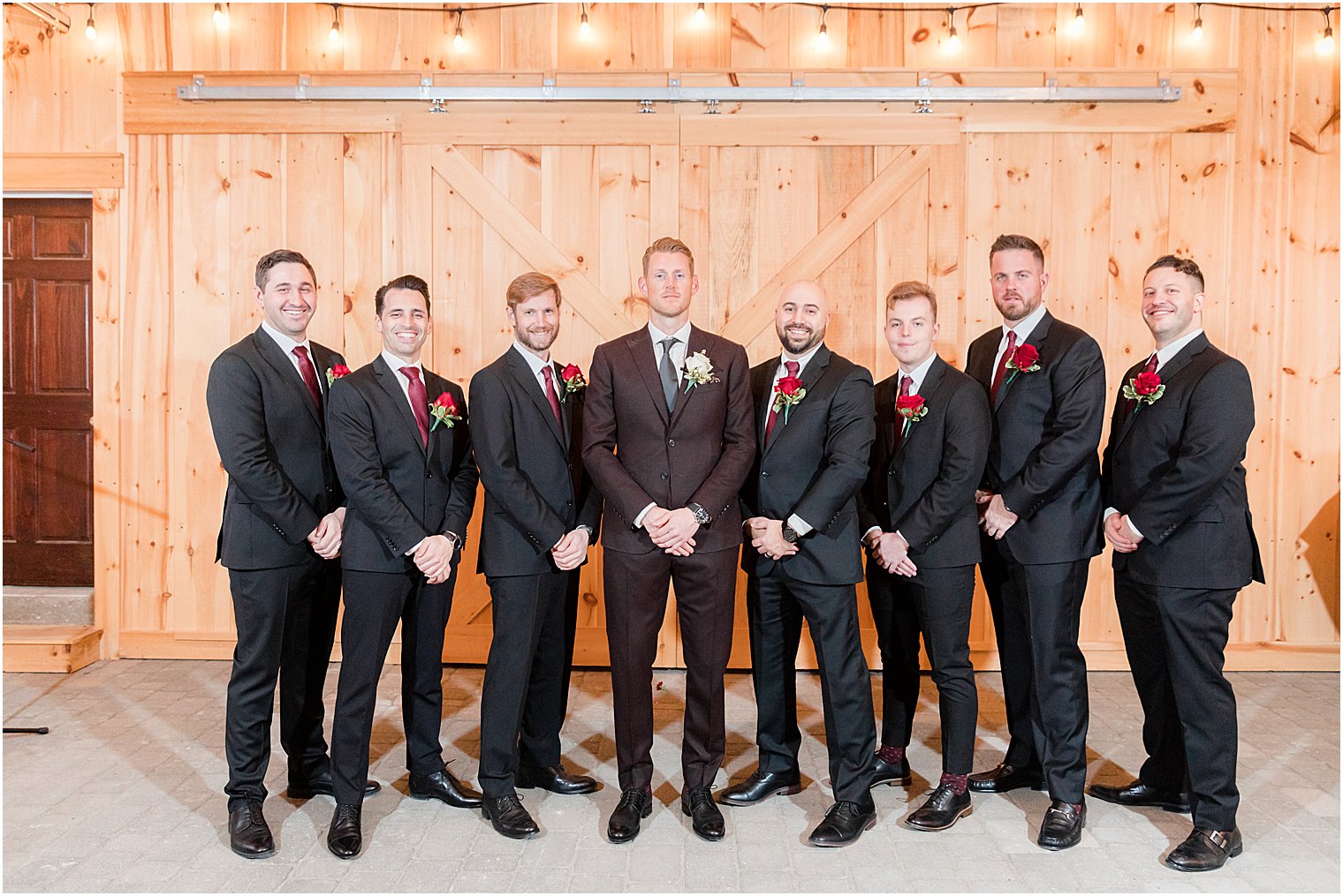 groom and groomsmen pose together by wooden wall