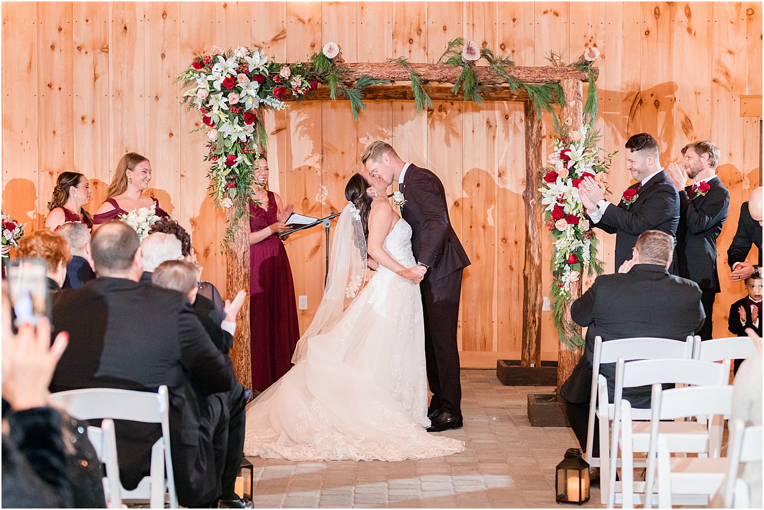 bride and groom kiss under wooden arbor at wedding ceremony in farmhouse