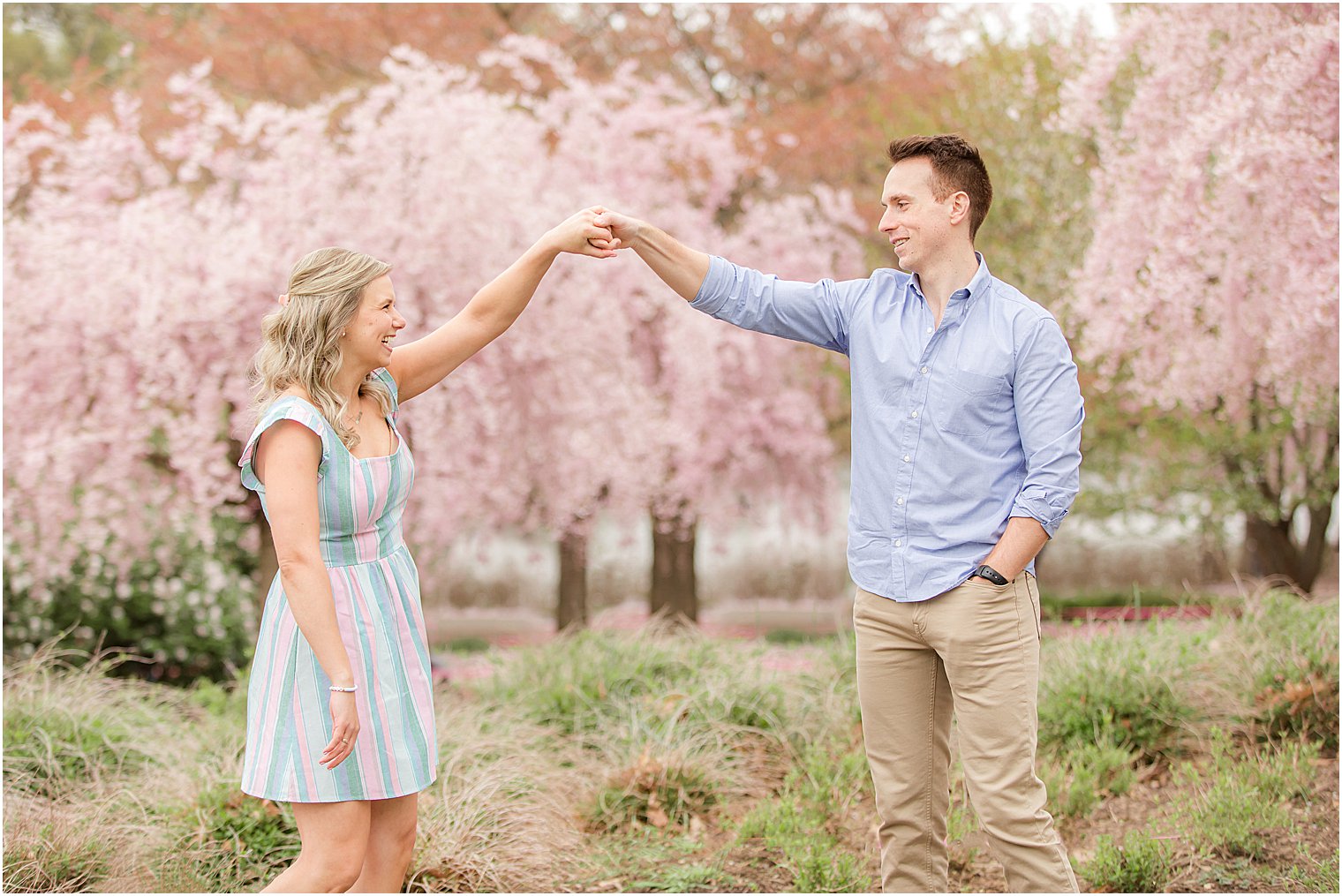 groom twirls bride by pink cherry blossom trees