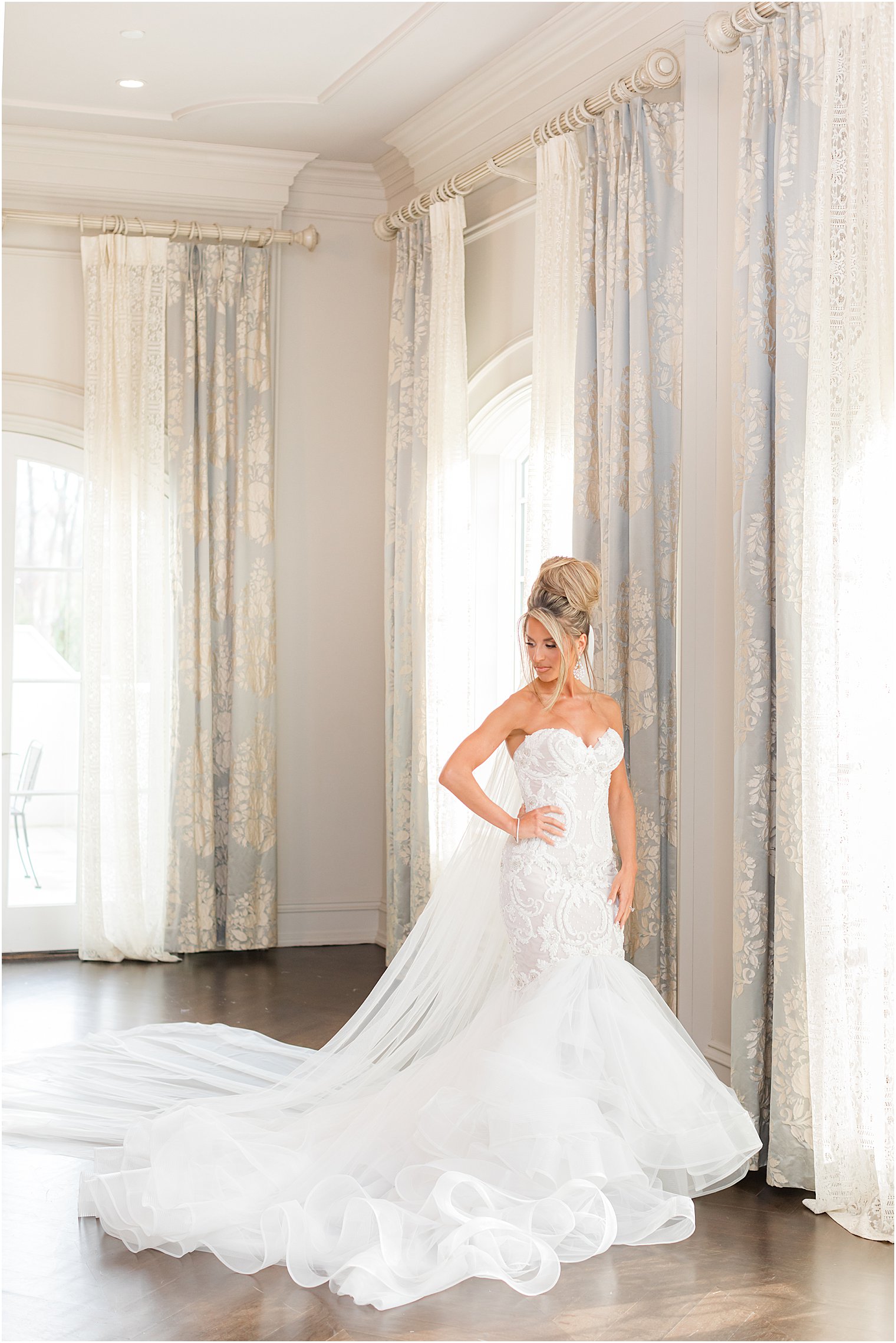 bride poses with wedding veil behind her and hand on hip looking out window