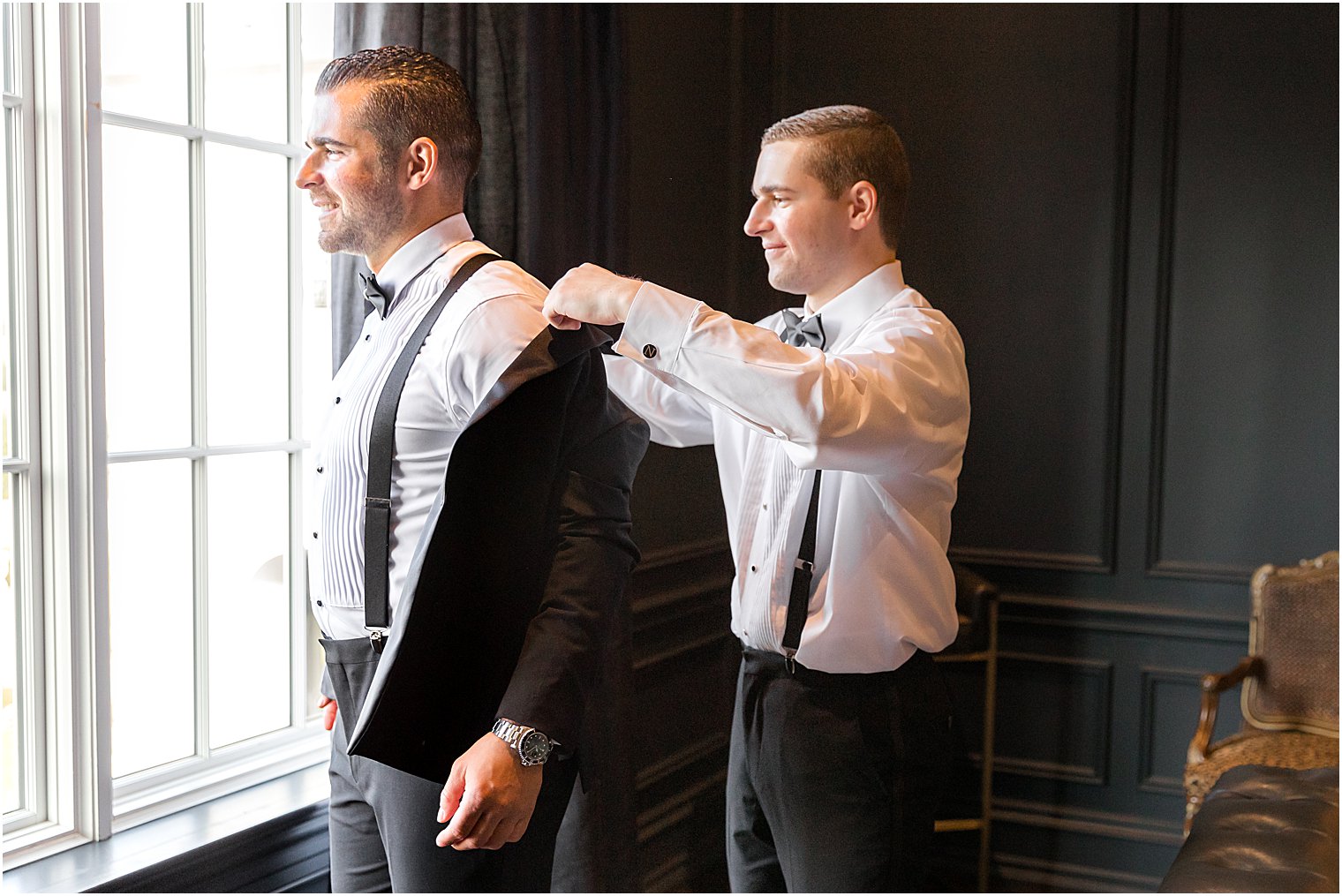 groomsman helps groom into tux jacket before winter Park Chateau Estate wedding
