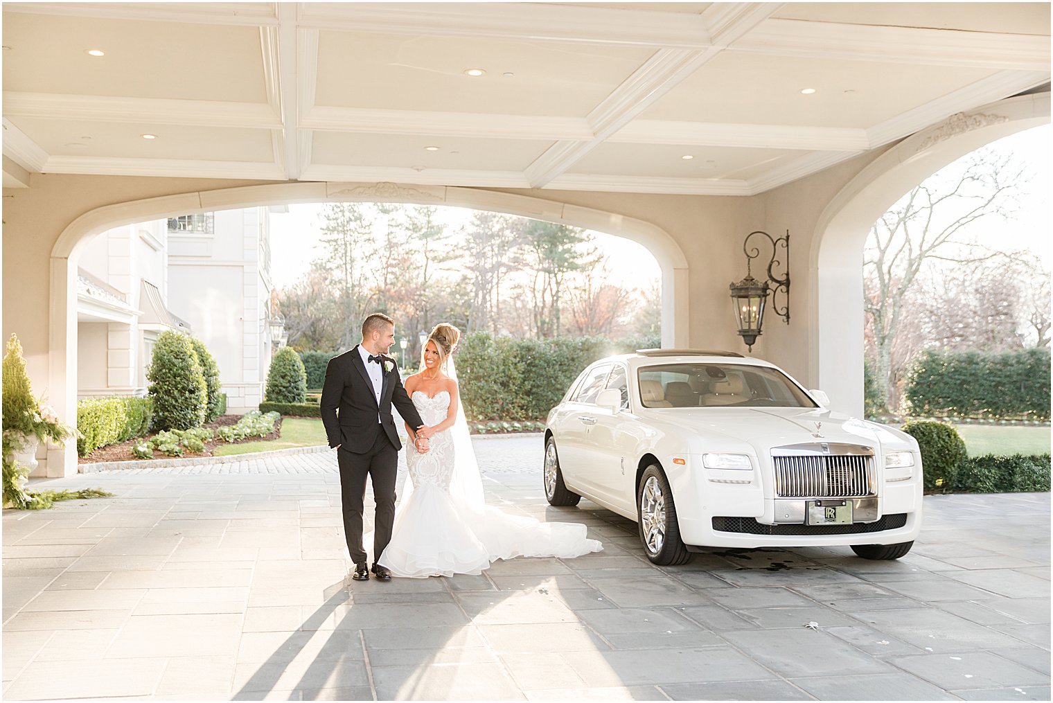 newlyweds hold hands walking by white Rolls Royce