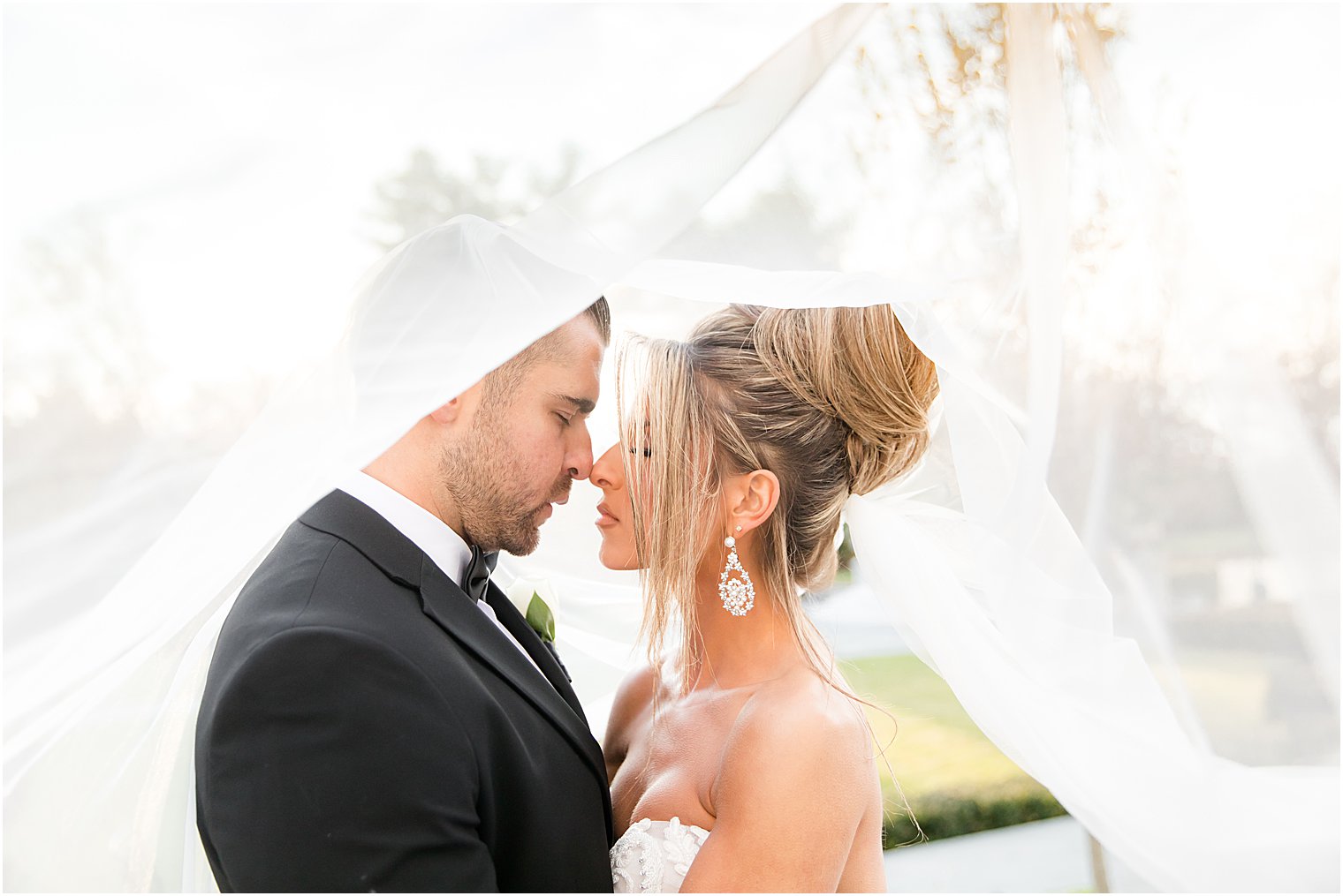 bride and groom touch noses under bride's veil during winter wedding portraits 