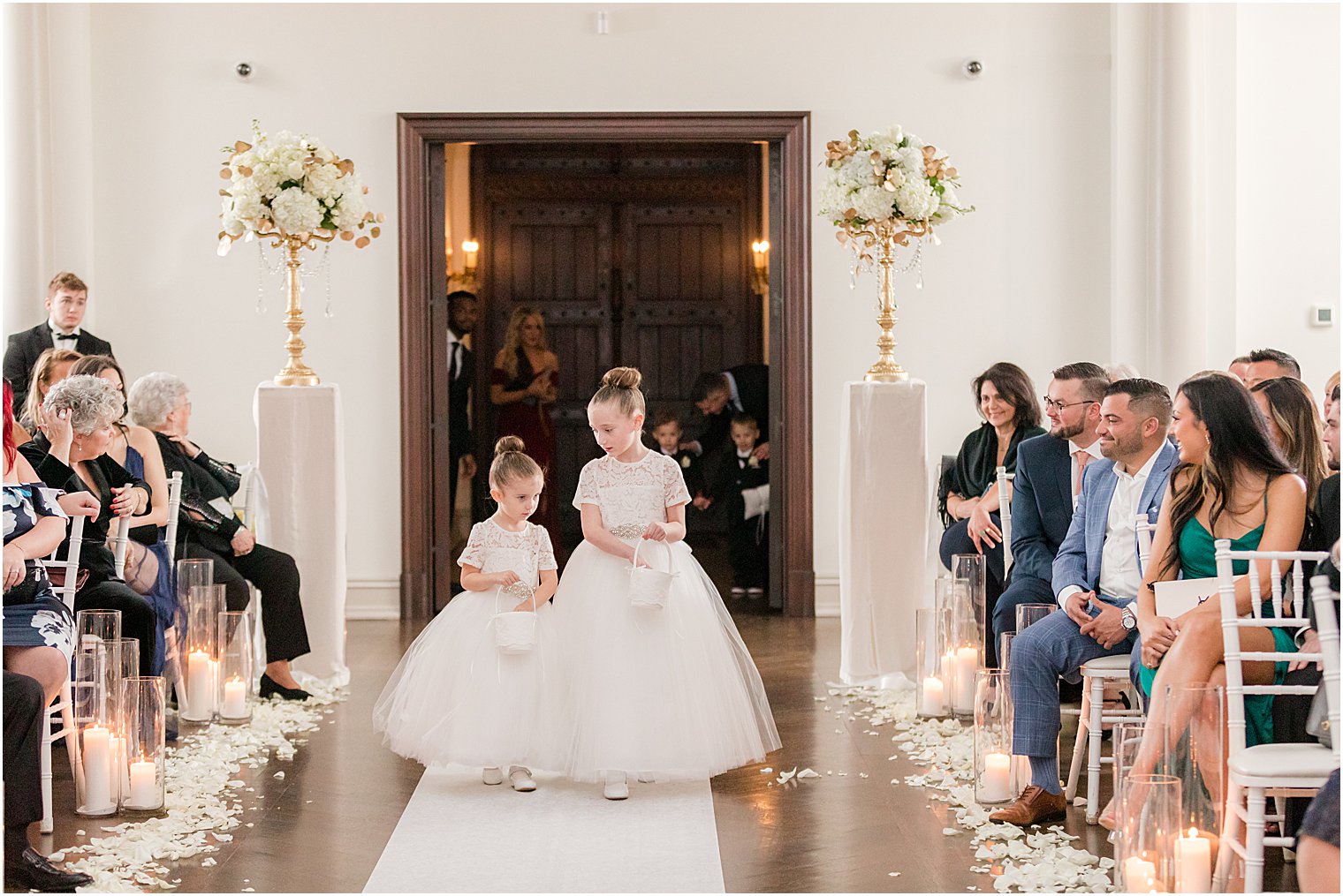 flower girls walk down aisle for winter wedding ceremony at twilight in Park Chateau Estate chapel