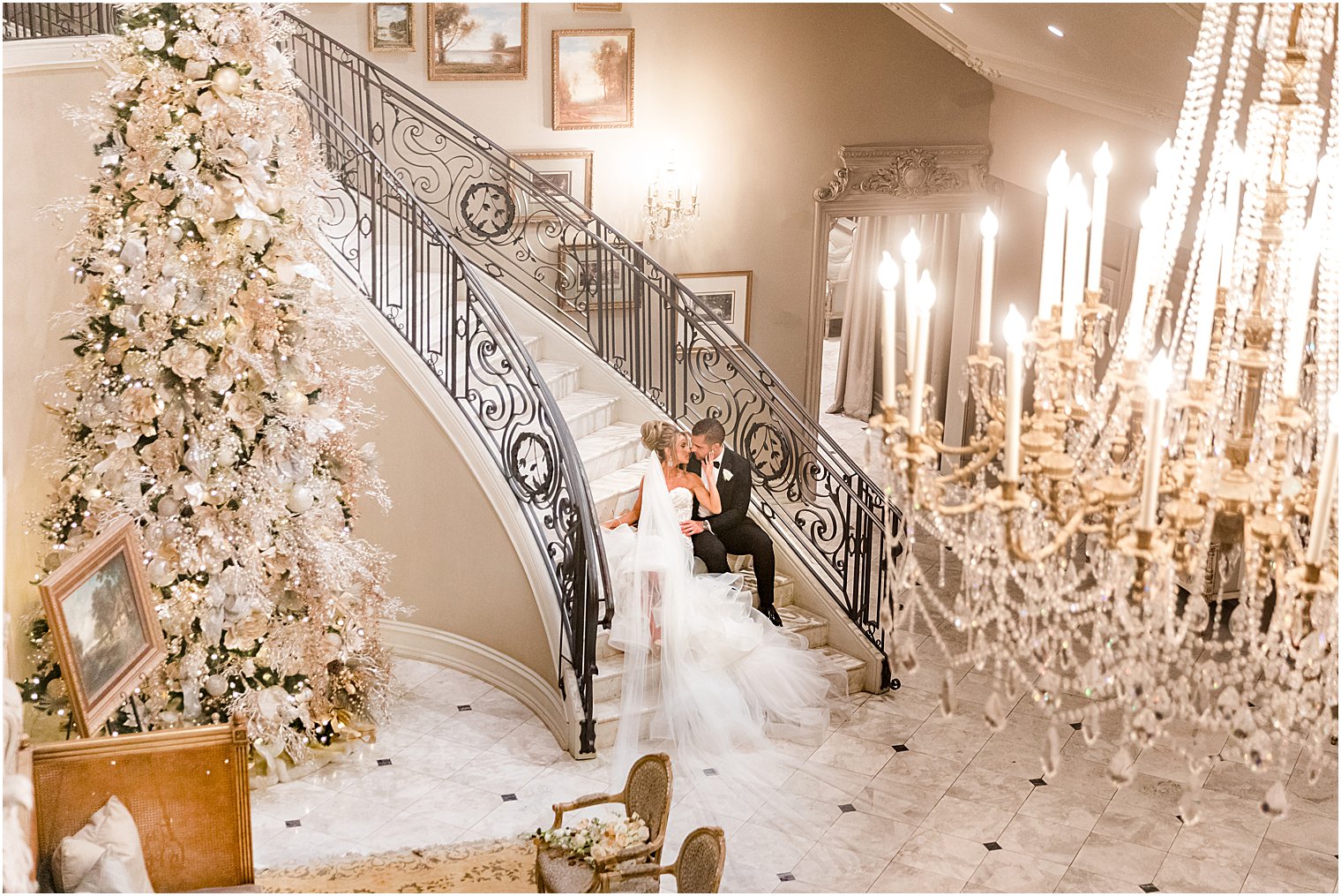 bride and groom sit on staircase at Park Chateau Estate with Christmas tree nearby 