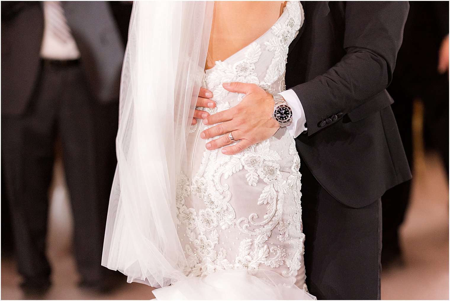 groom holds bride's hip on lace wedding gown