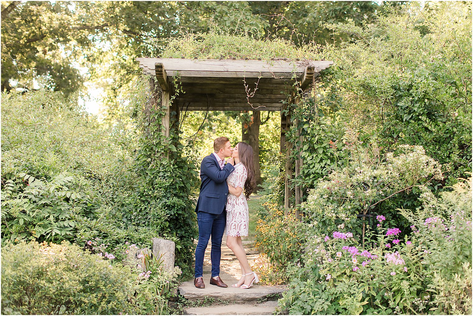 engaged couple kisses under wooden arbor at Skylands Manor
