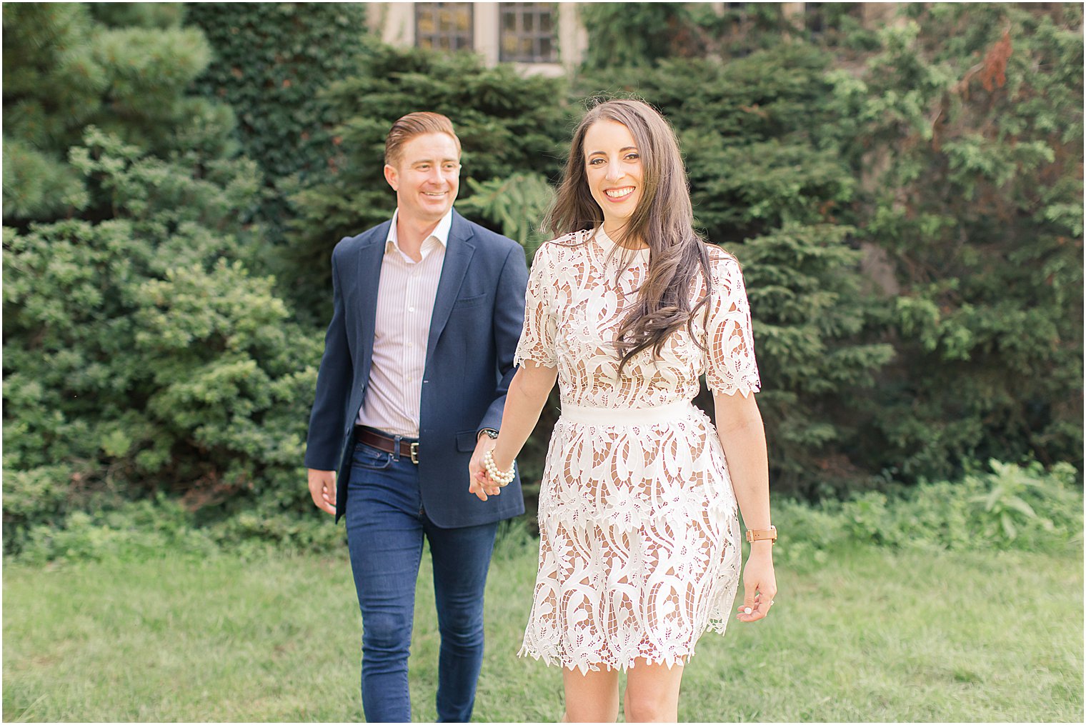 woman leads man walking during summer engagement session at Skylands Manor