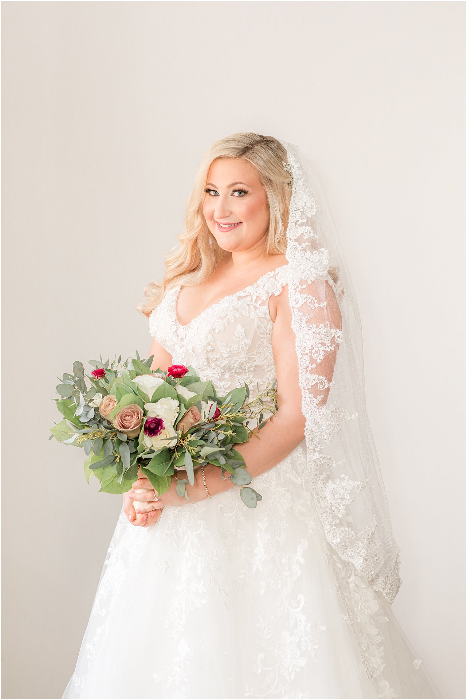 bride holds bouquet of white and red flowers with veil around shoulders