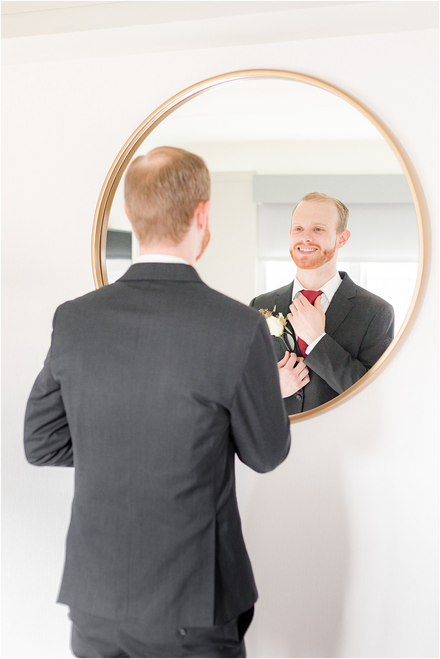 groom adjusts tie in mirror before NJ wedding