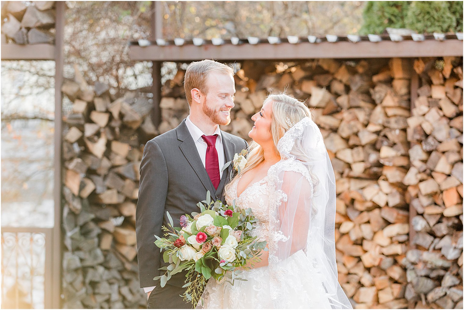 newlyweds smile together by wood pile at Stone House at Stirling Ridge