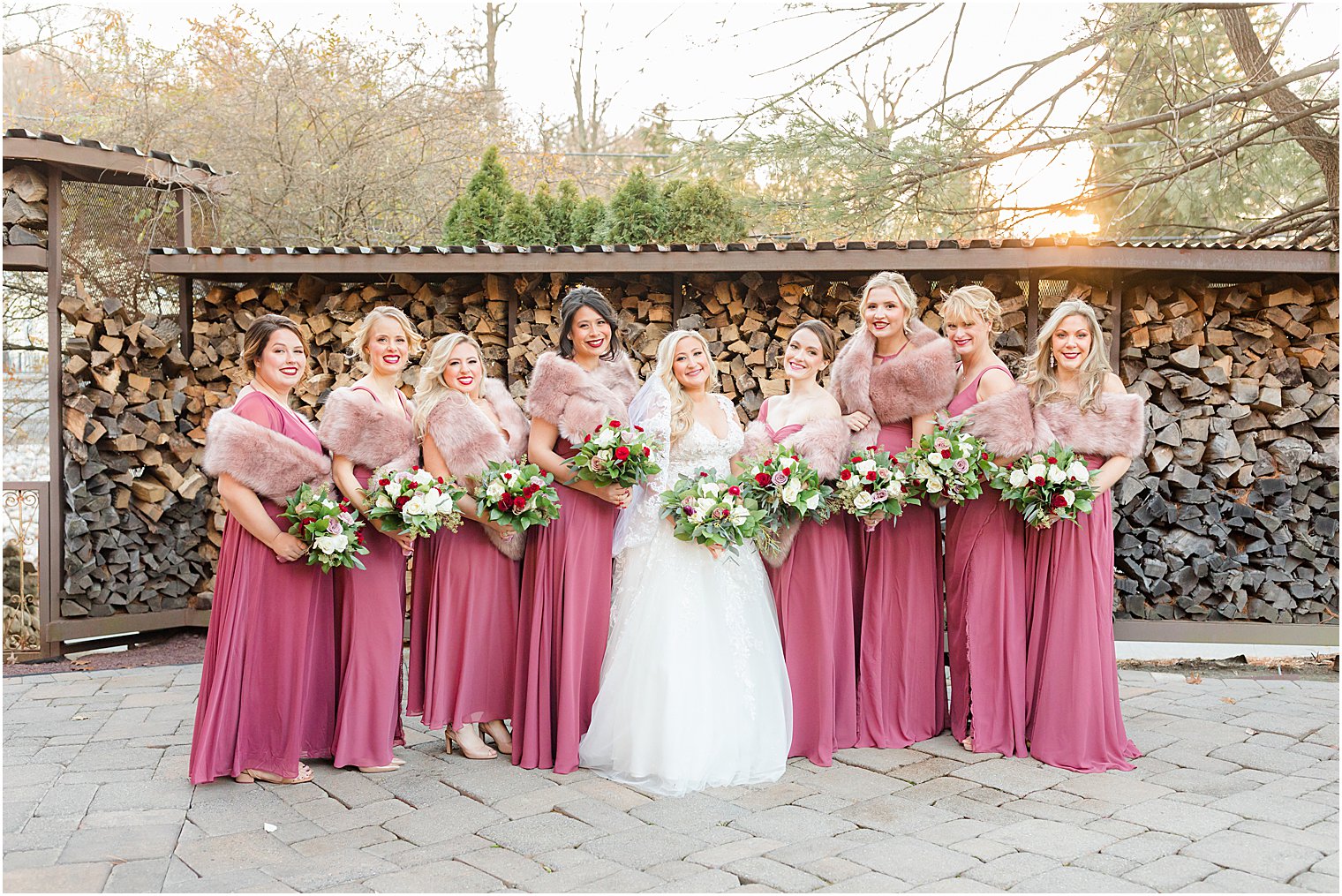 bride and bridesmaids pose along wood pile at Stone House at Stirling Ridge