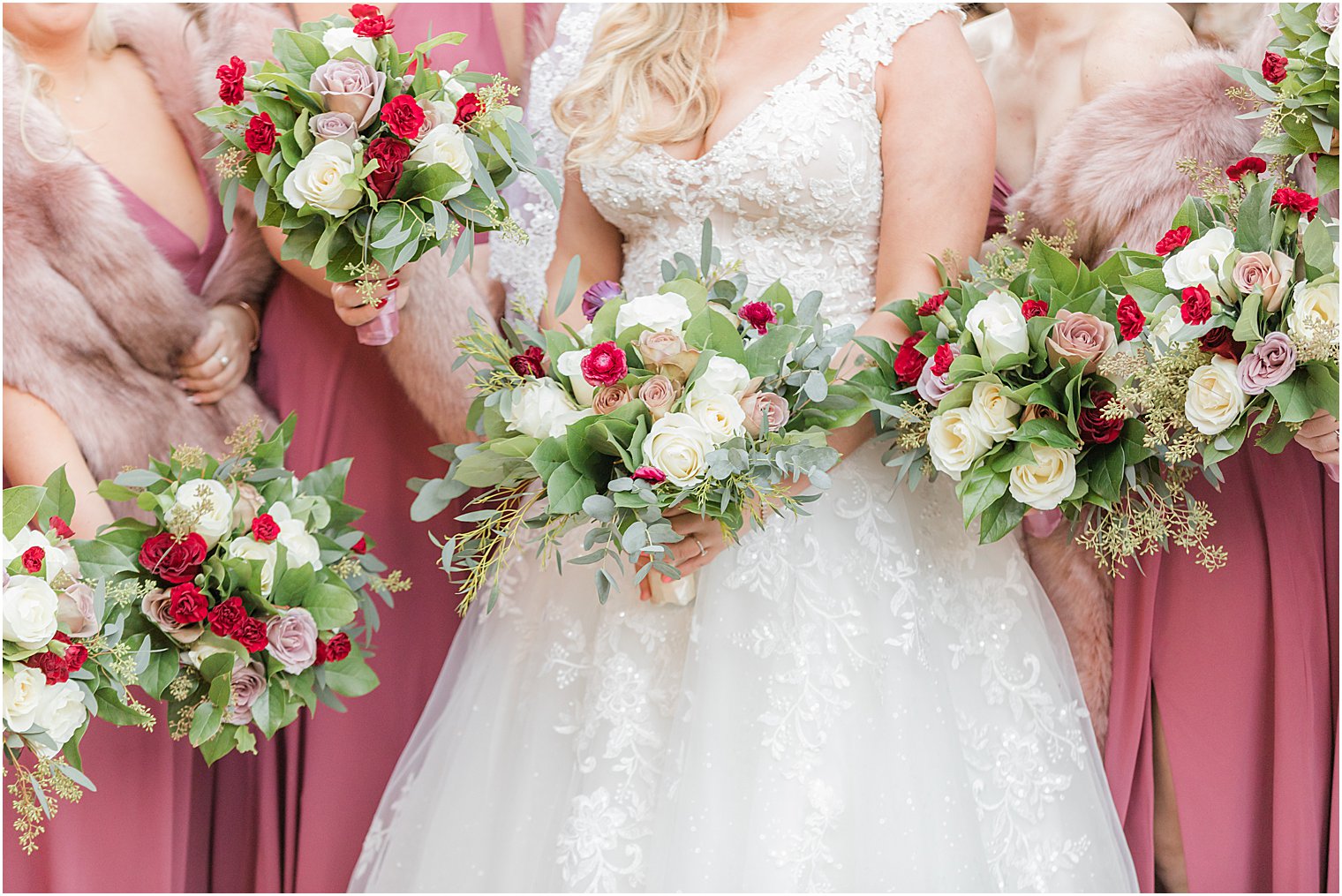 bride and bridesmaids hold bouquets of white and red flowers