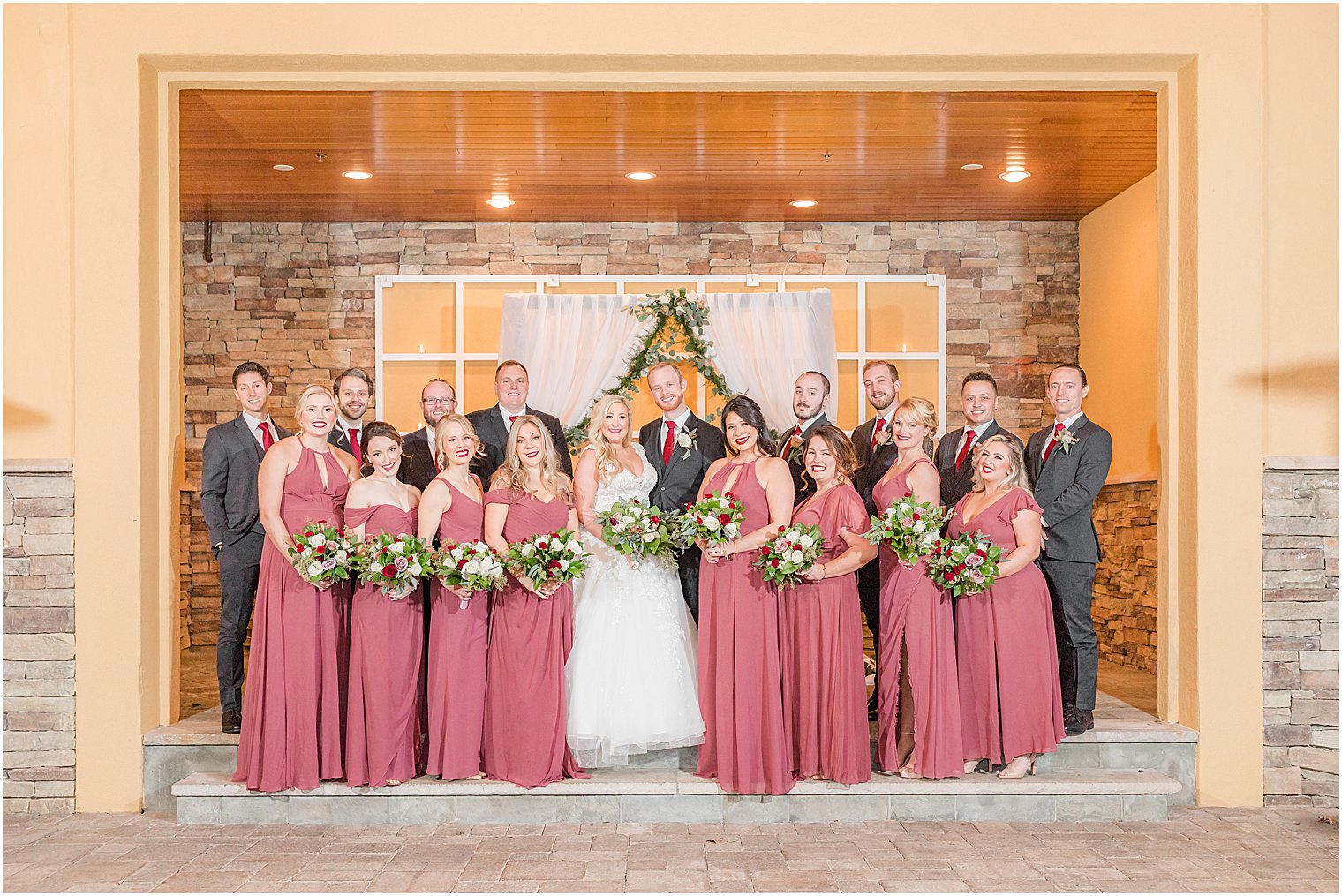 bride and groom pose with wedding party by arbor at Stone House at Stirling Ridge