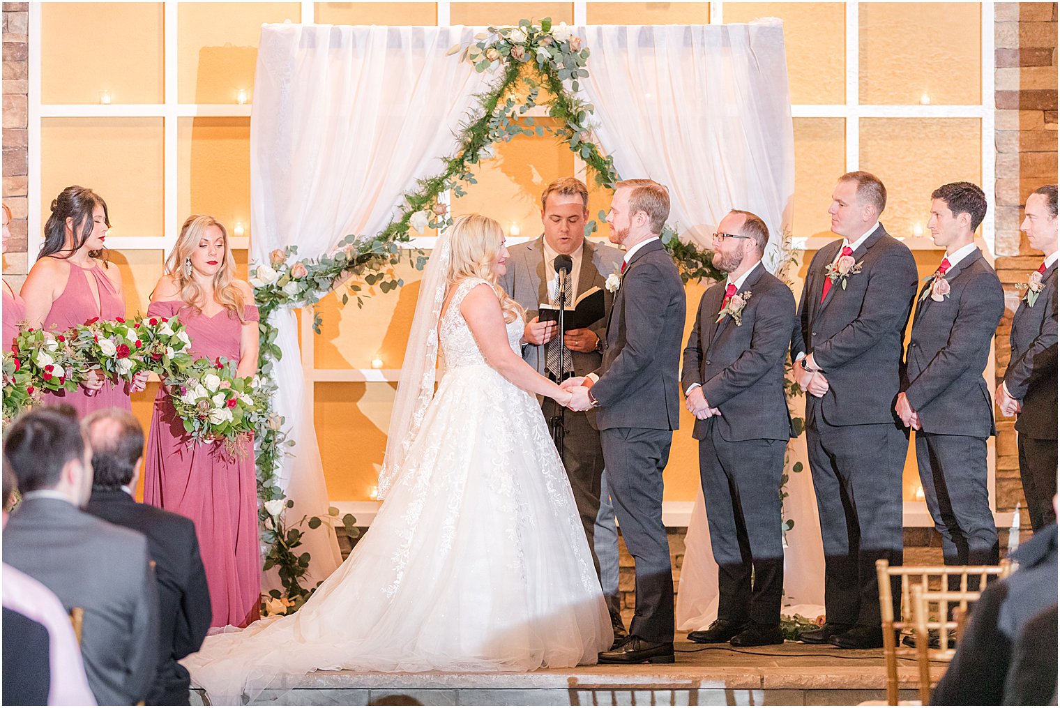 bride and groom hold hands during fall wedding ceremony under arbor with greenery