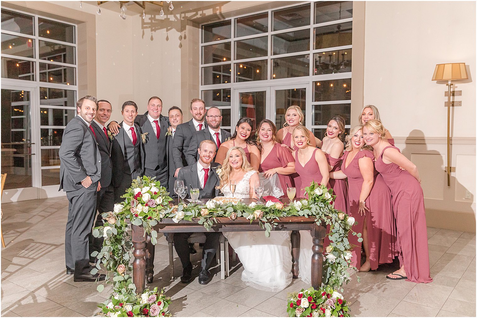 newlyweds sit at sweetheart table with wedding party around them