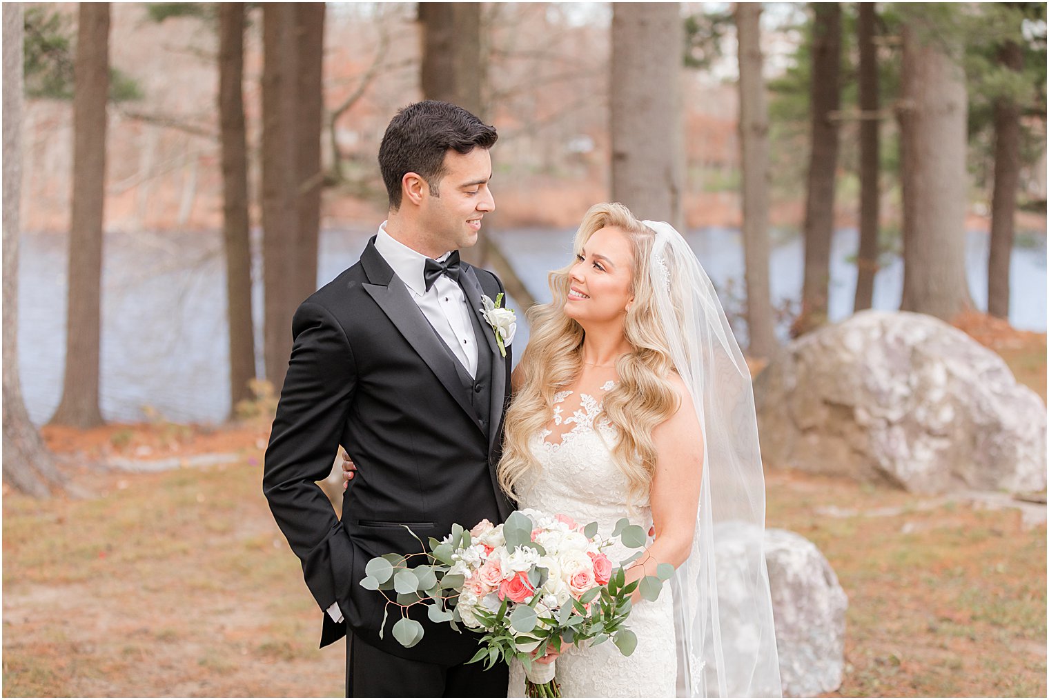 bride and groom smile together during winter wedding portraits in woods 