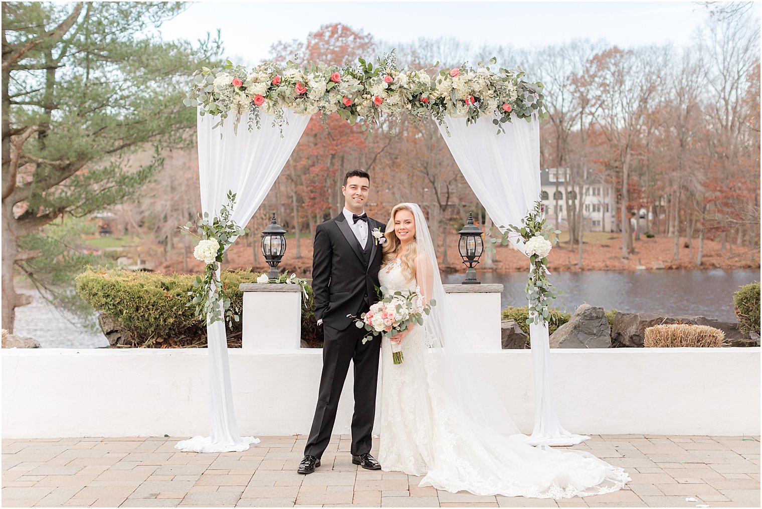 newlyweds pose under floral arbor on the patio at the Estate at Farmington Lake