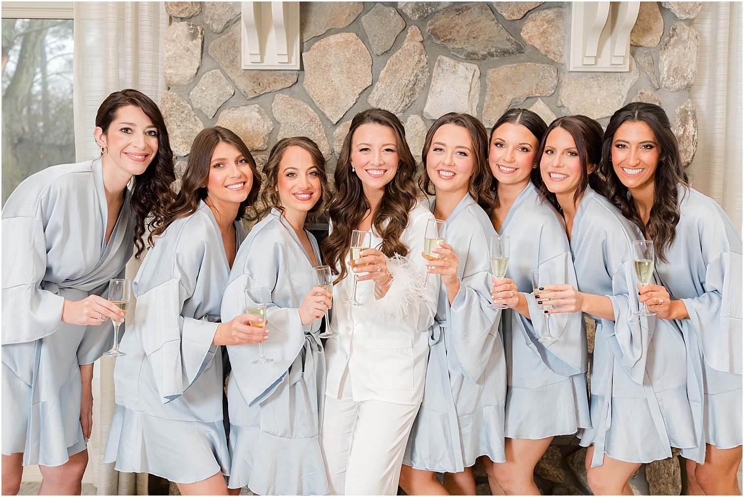 bridesmaids in blue pajamas pose by stone fireplace