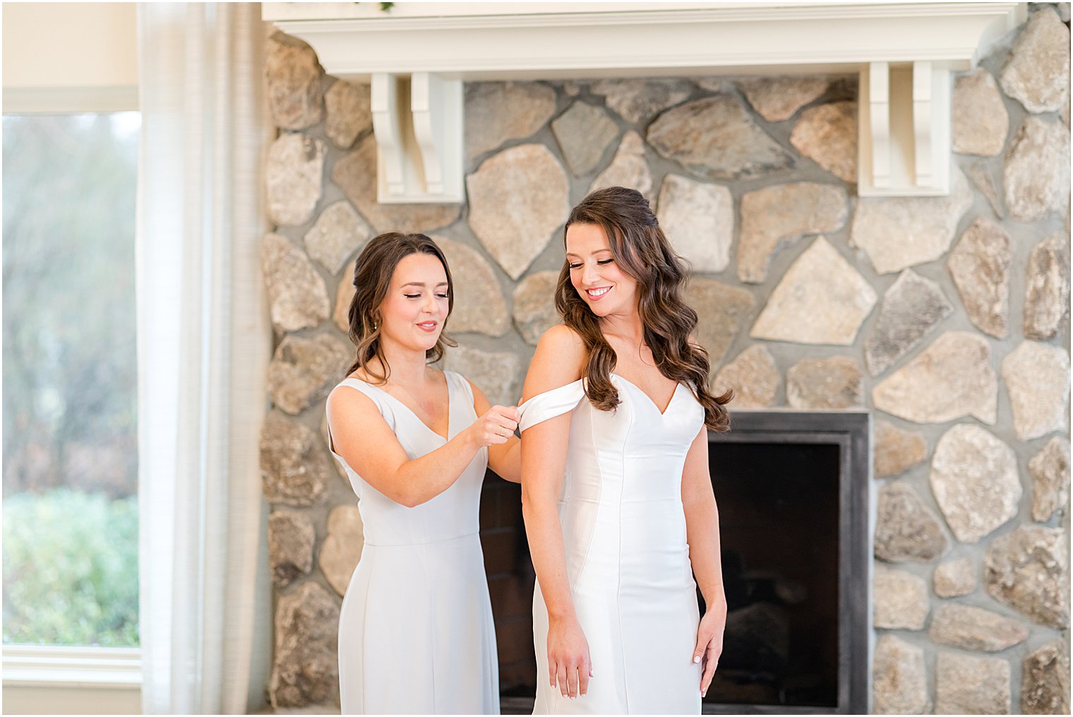 bridesmaid helps bride with sleeve of wedding gown