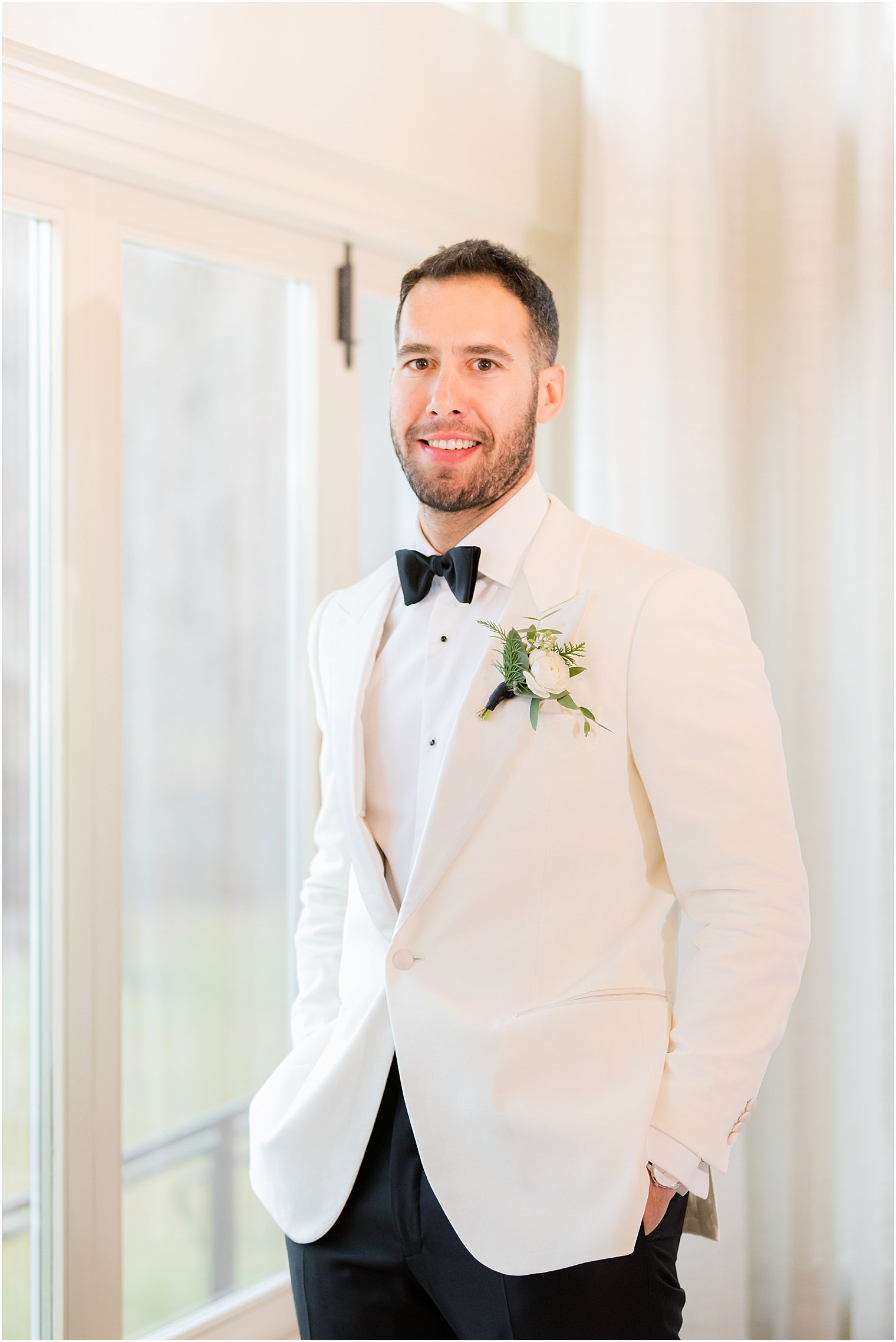 groom stands with hands in pockets wearing white tux jacket
