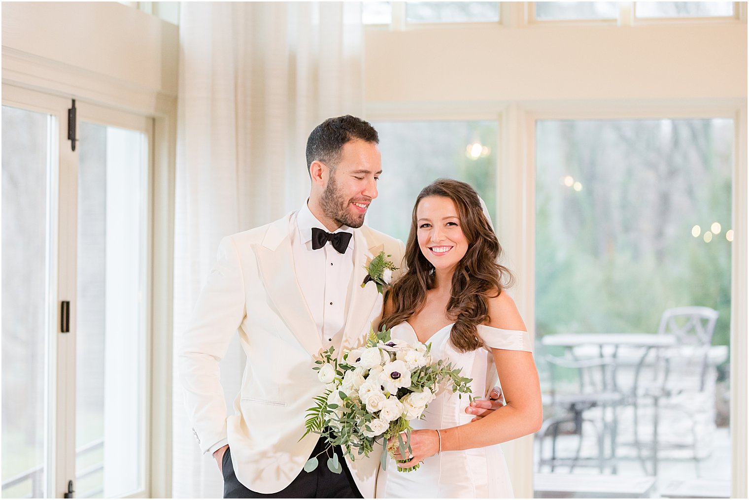 groom looks down at bride standing in room with windows at Indian Trail Club