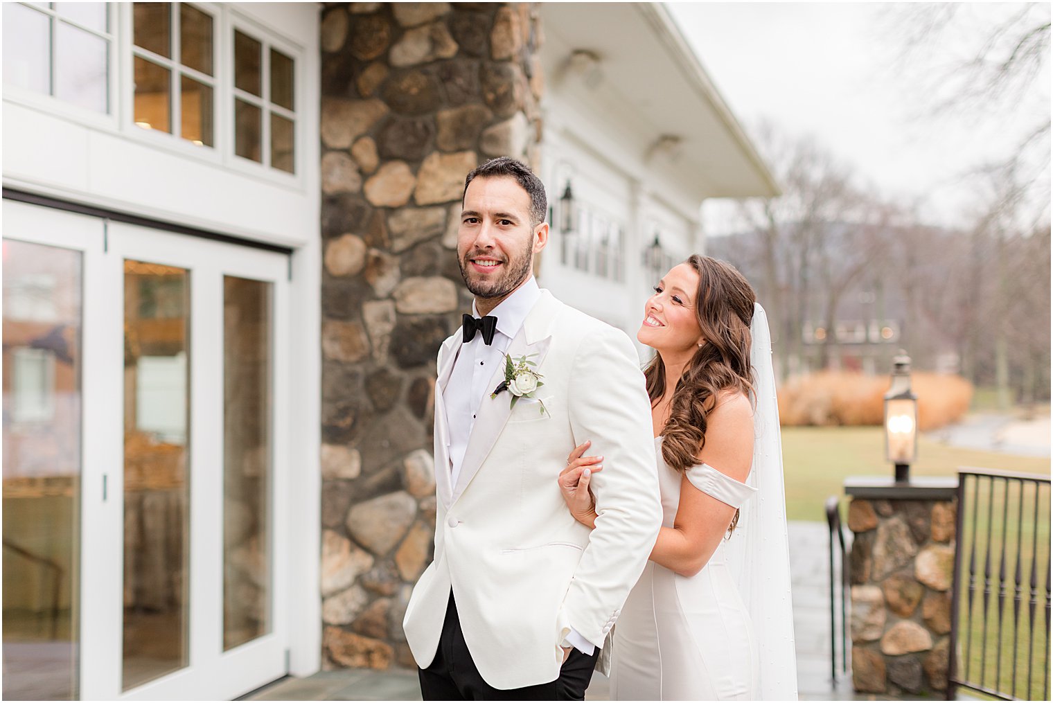 bride stands behind groom hugging him