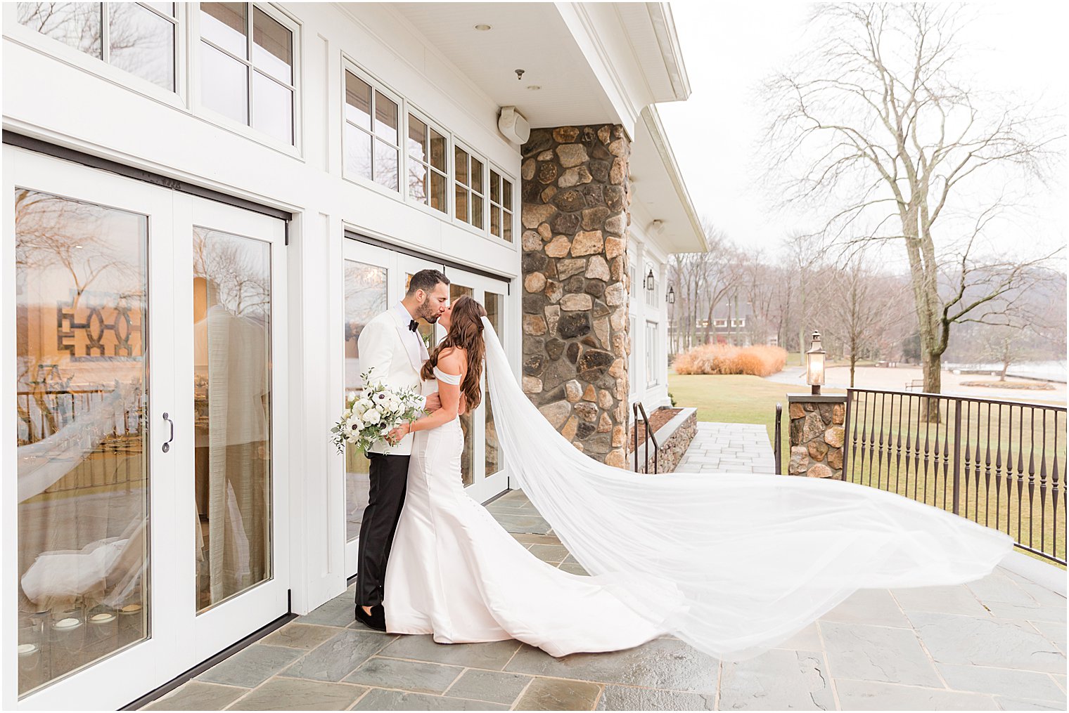 bride and groom kiss with bride's veil floating behind her