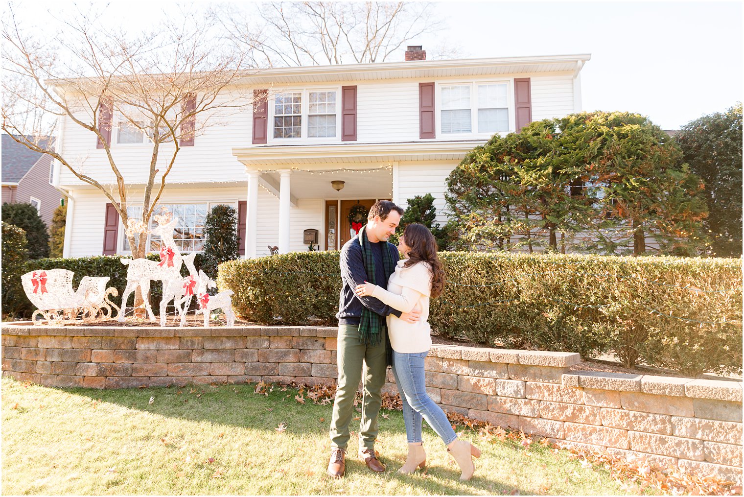 bride and groom hug on front lawn of home during holiday engagement session
