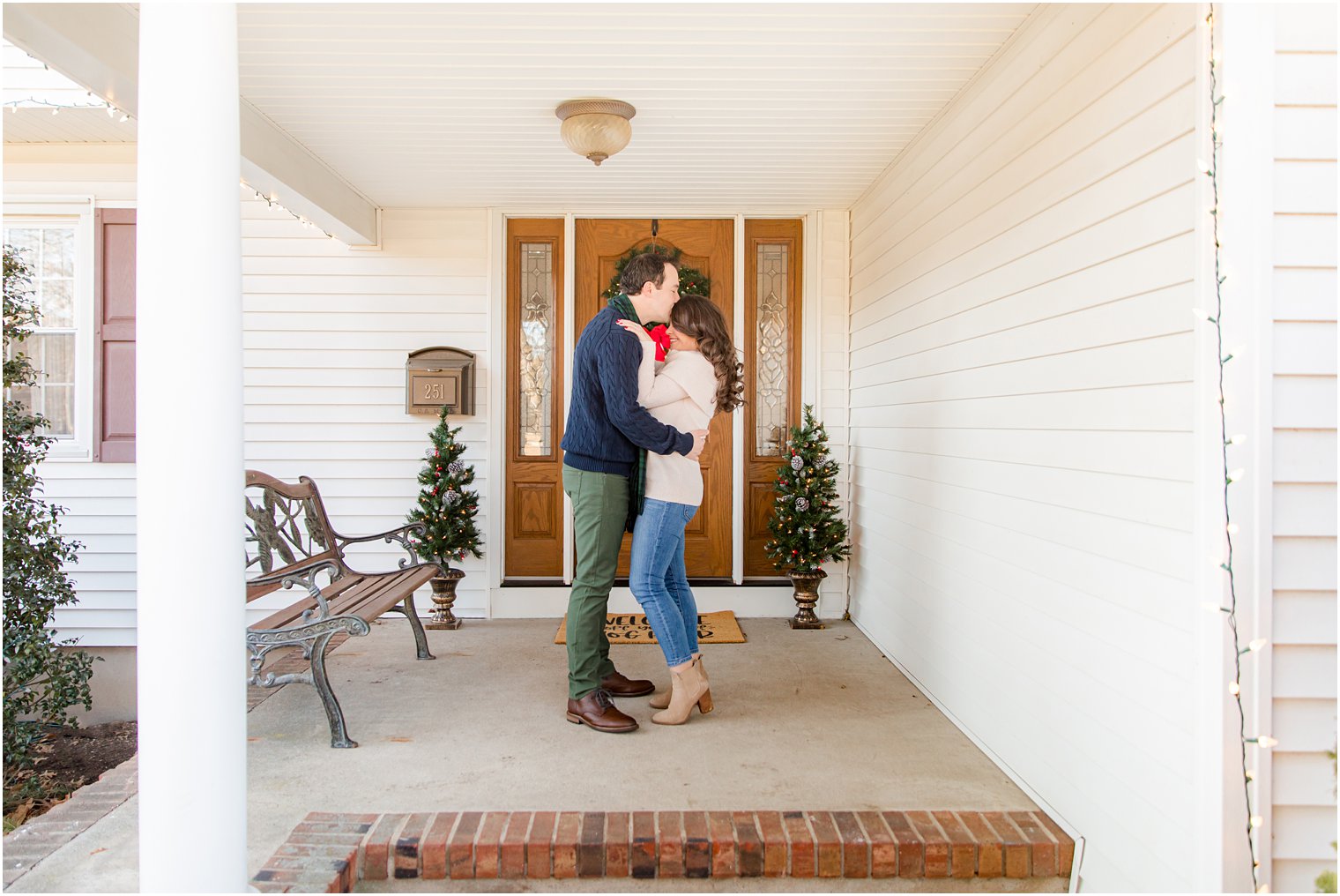 bride and groom stand on front porch during winter engagement photos 