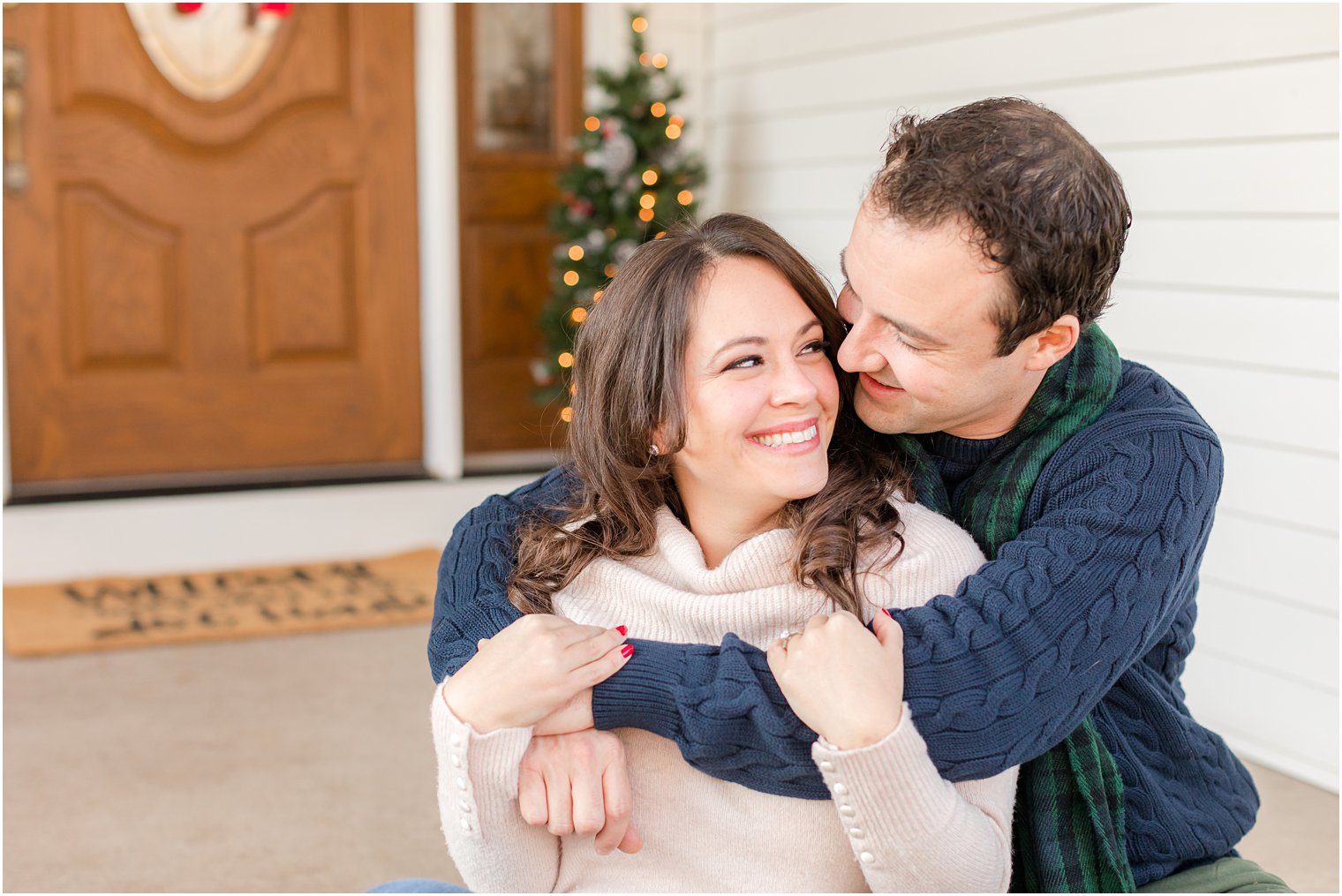 groom hugs bride sitting on front step during winter engagement photos 