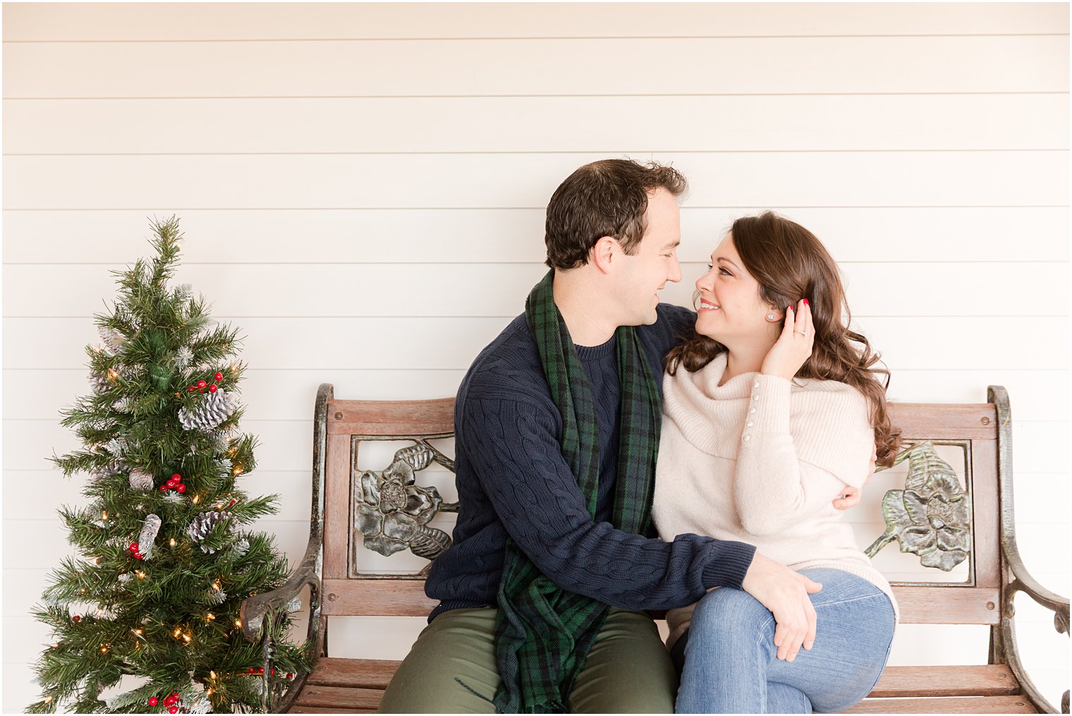 bride and groom sit on front porch next to small Christmas tree during holiday engagement photos