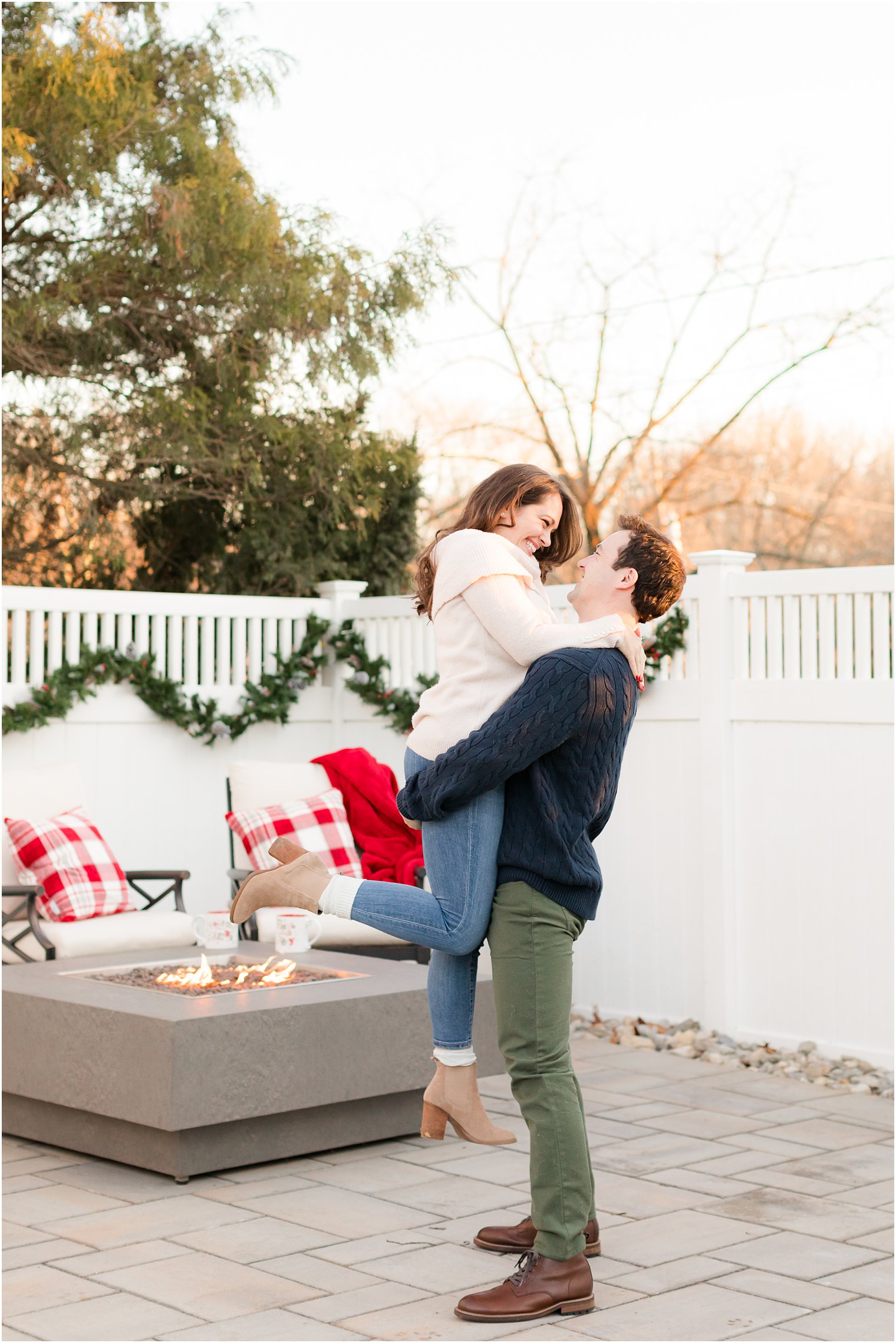groom lifts bride up on patio during at home holiday engagement photos