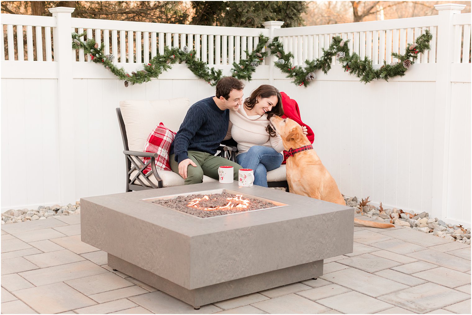 bride and groom sit with dog on patio during holiday inspired engagement session at home 