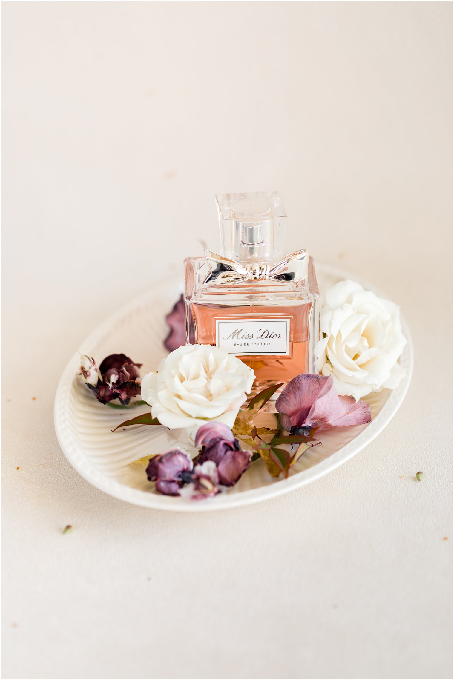 bride's Miss Dior perfume bottle rests in shell dish with purple flowers 