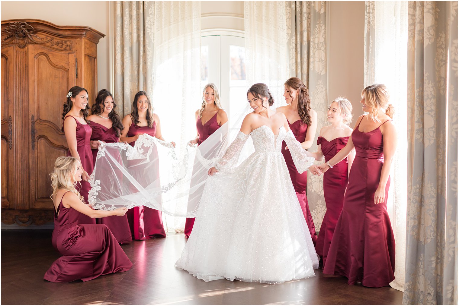 bridesmaids in burgundy gowns help bride prepare for NJ wedding day