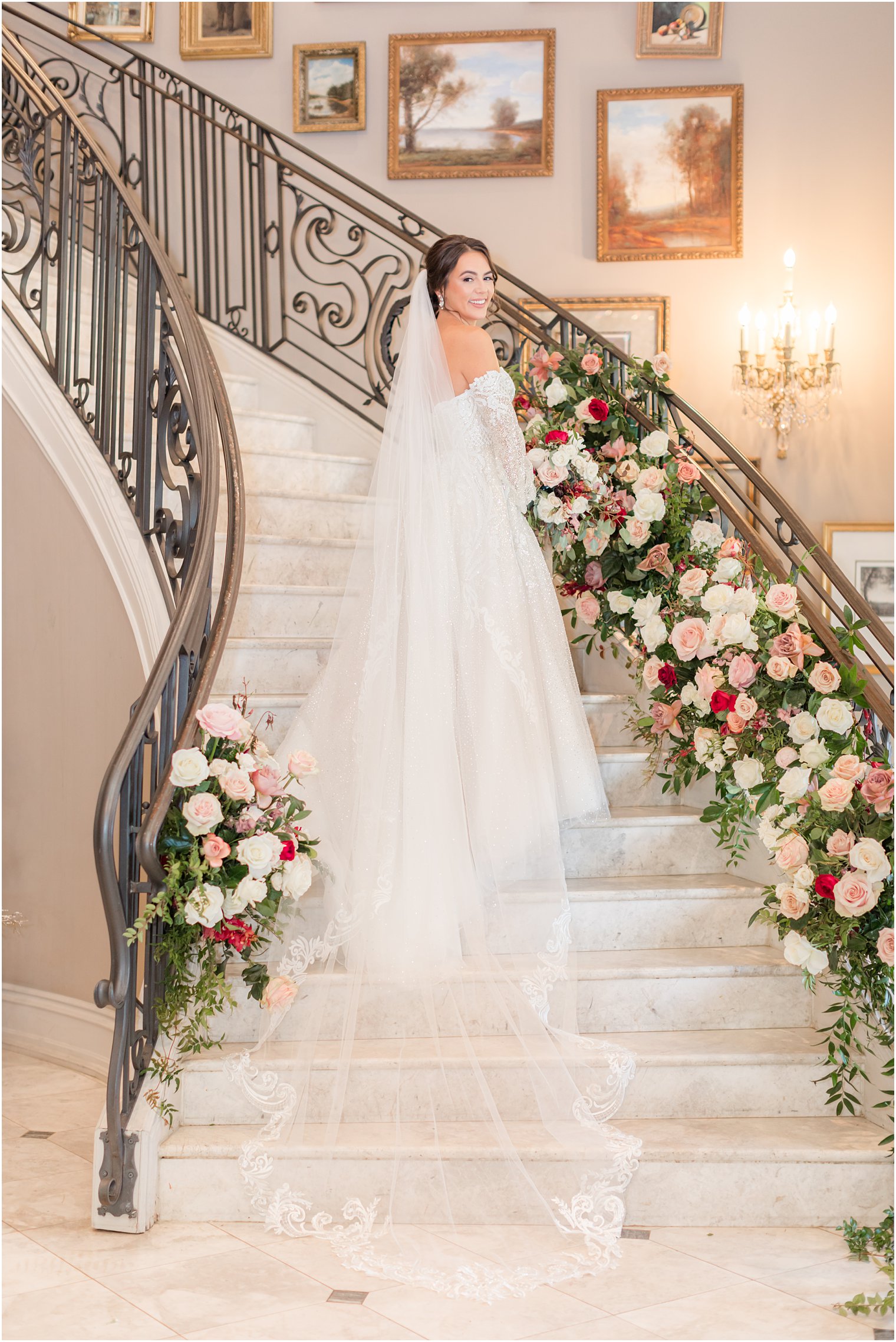 bride stands on grand staircase at Park Chateau Estate with veil flowing down steps behind her 