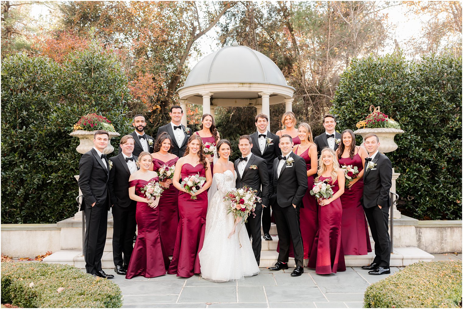 bride and groom pose with wedding party in black and burgundy in gardens at Park Chateau Estate