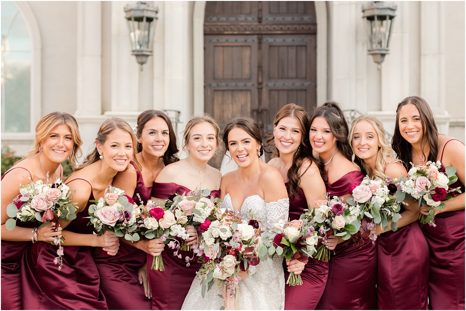bride smiles with bridesmaids in burgundy gowns outside Park Chateau Estate chapel 