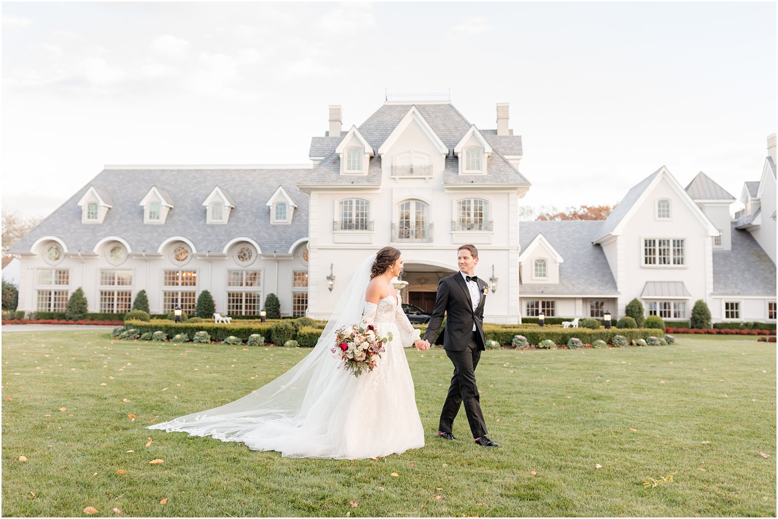 newlyweds hold hands walking through front lawn at Park Chateau Estate
