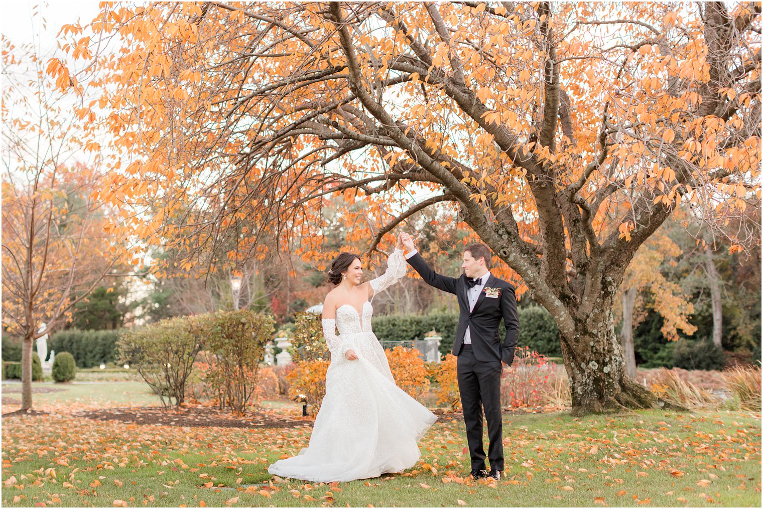 groom twirls bride under tree with orange leaves on the lawn at Park Chateau Estate