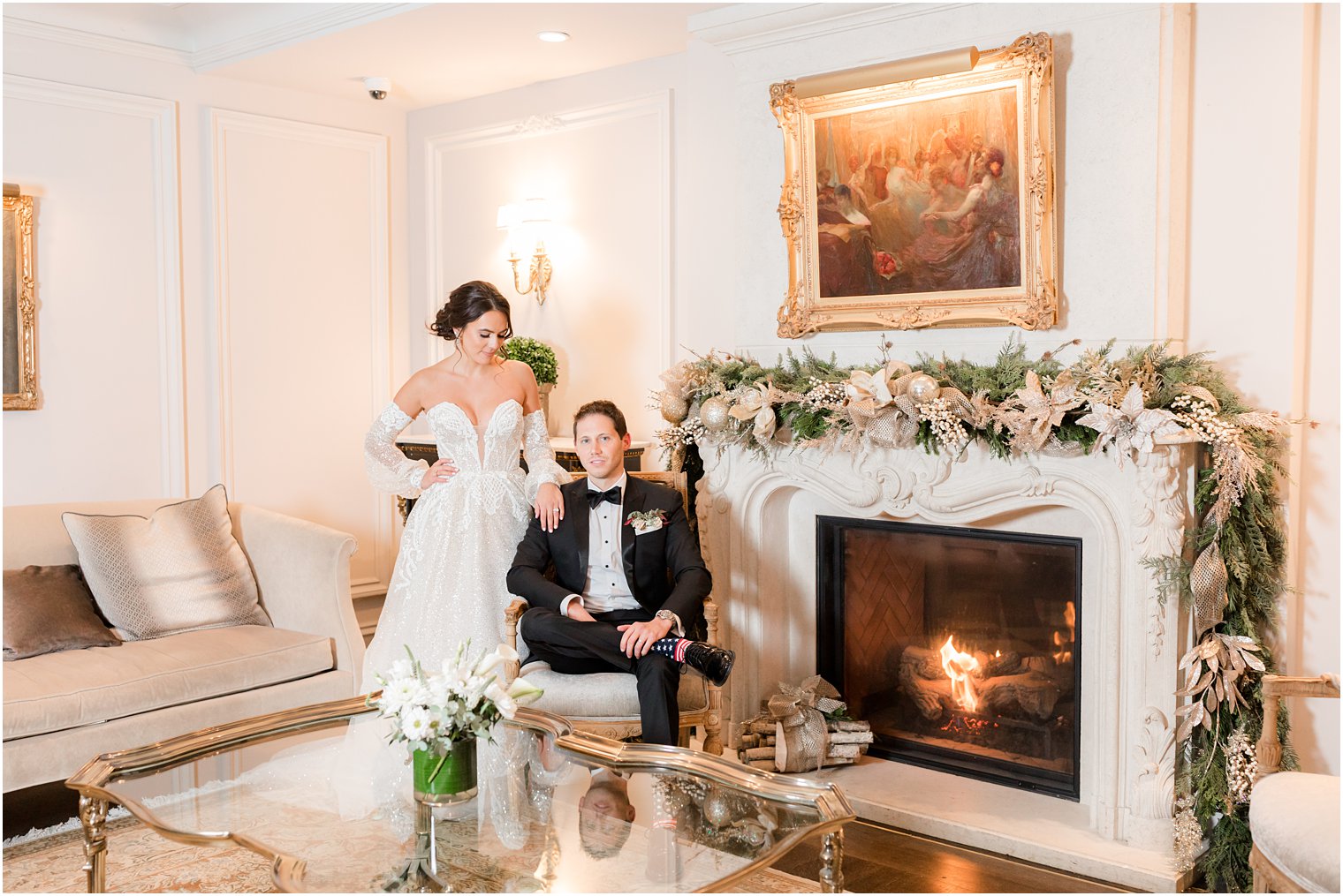 groom sits by fireplace at Park Chateau Estate with bride standing behind him 