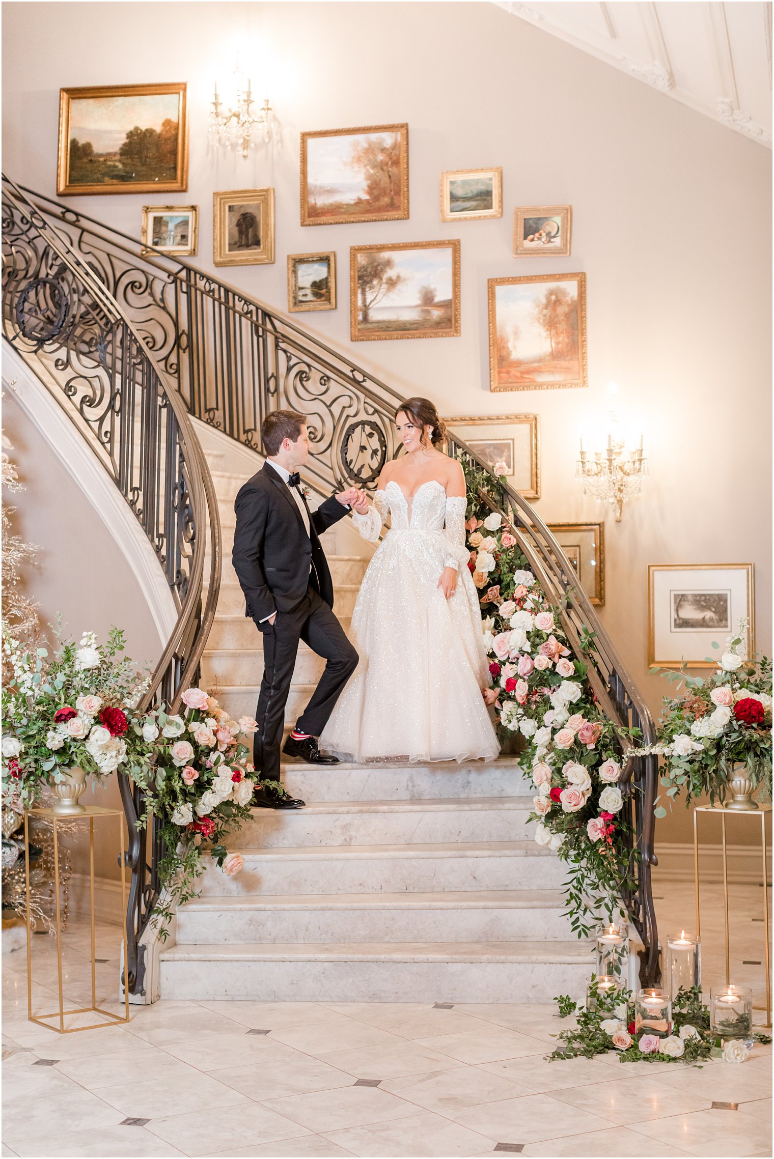 bride and groom walk down grand staircase with pink and white flowers on the railings at Park Chateau Estate