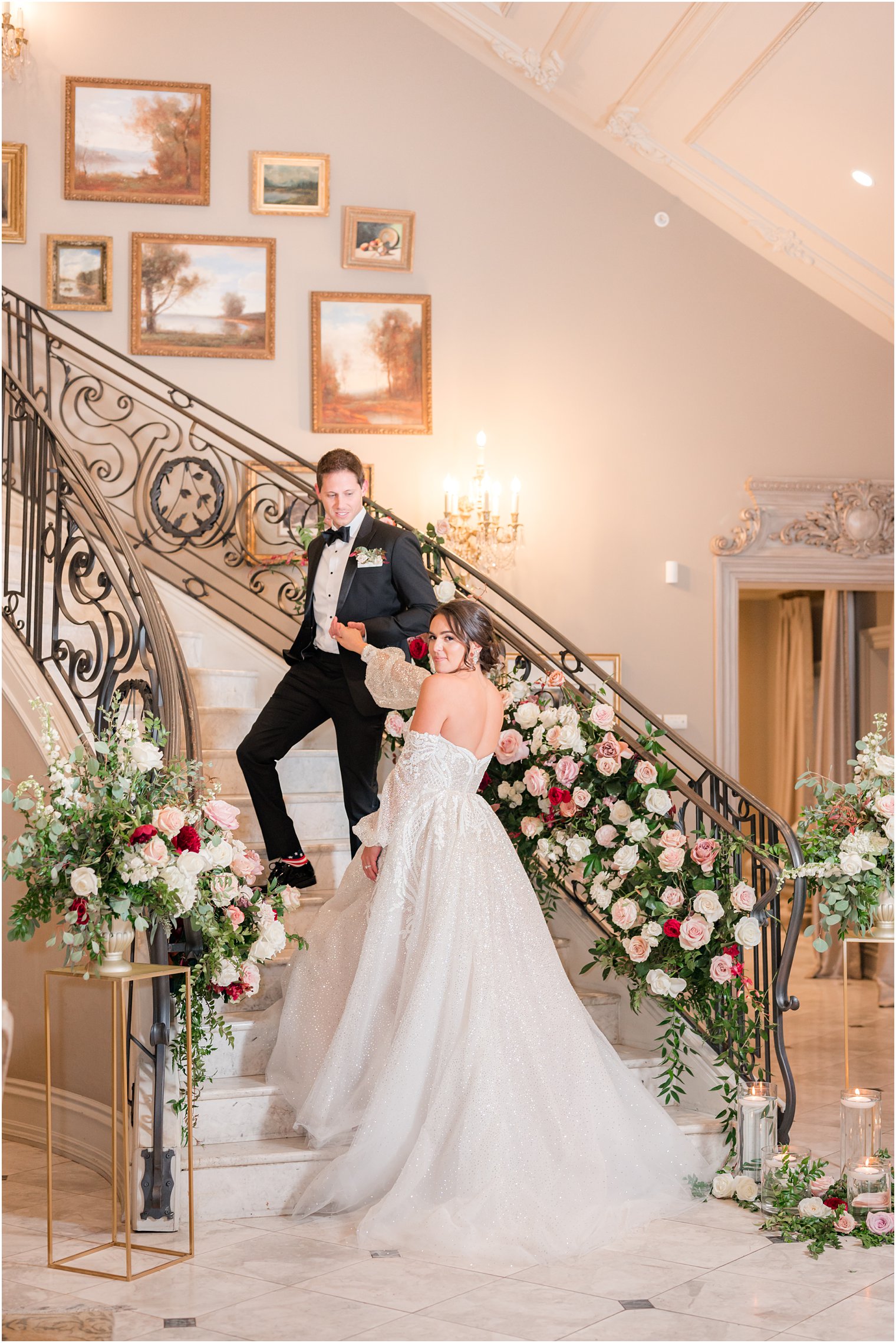 groom leads bride up staircase at Park Chateau Estate with florals down railings 