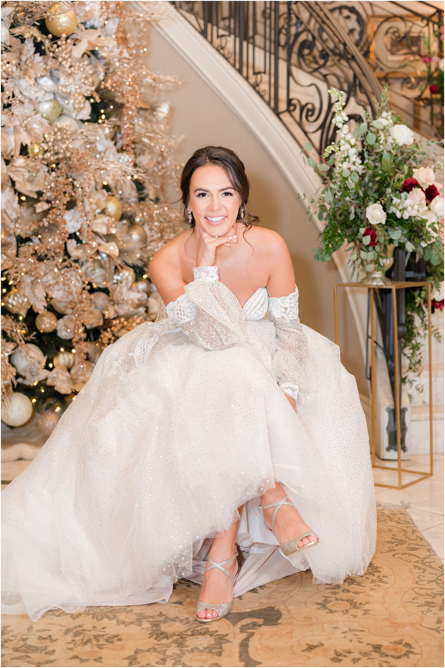 bride sits by Christmas tree in strapless wedding gown with detachable sleeves