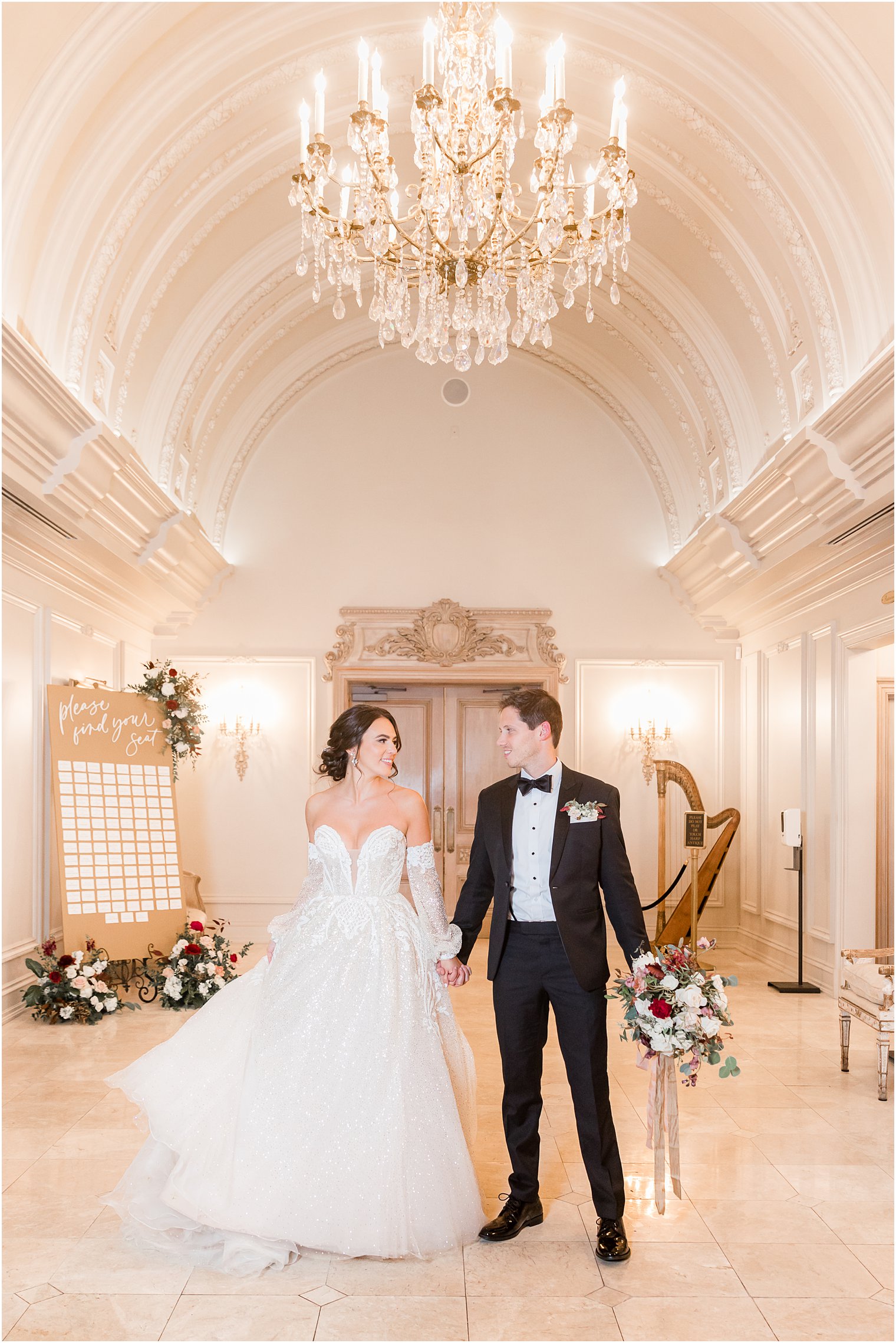 newlyweds hold hands in hallway in front of seating chart before NJ wedding reception 