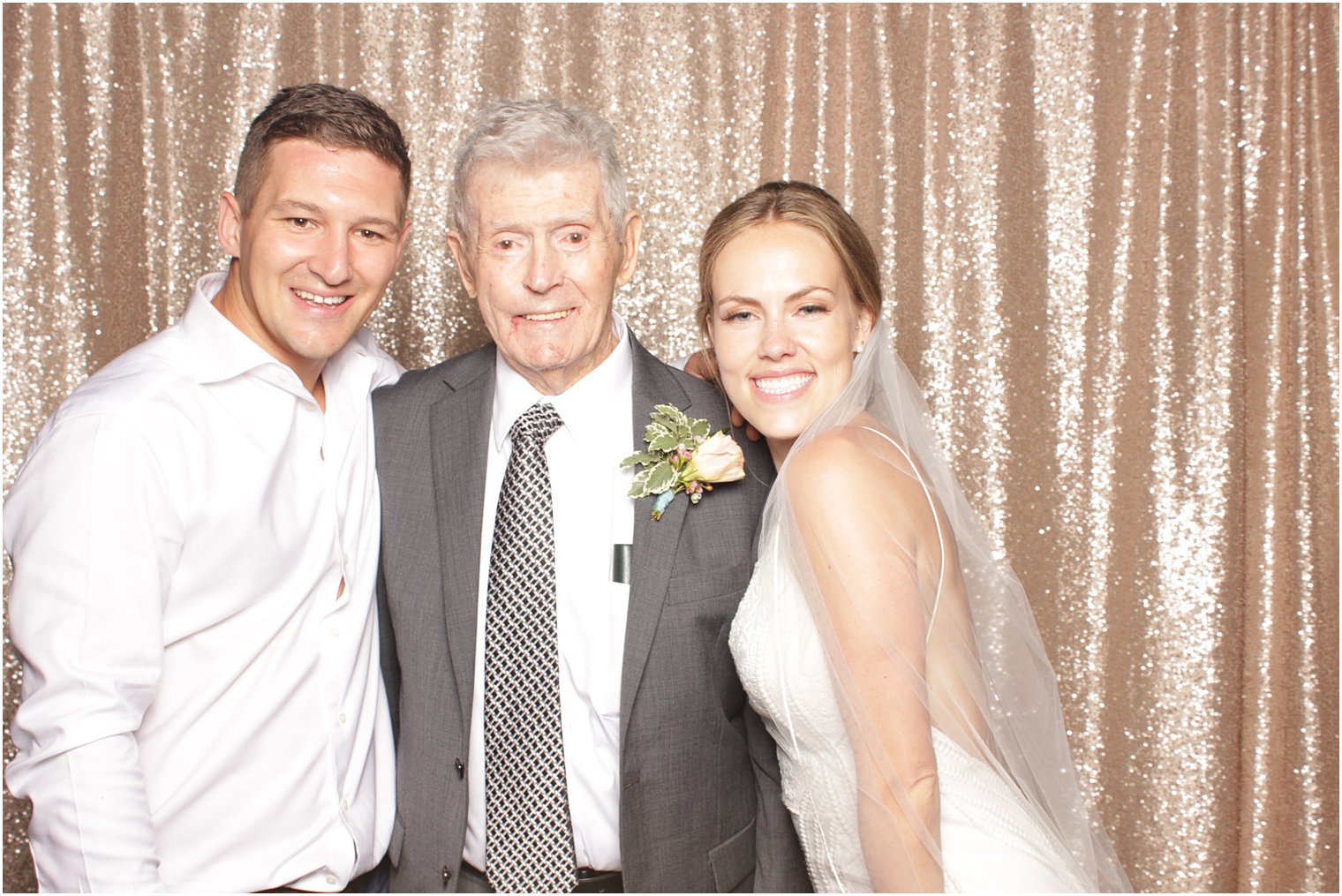 bride and groom smile with grandfather in photo booth 
