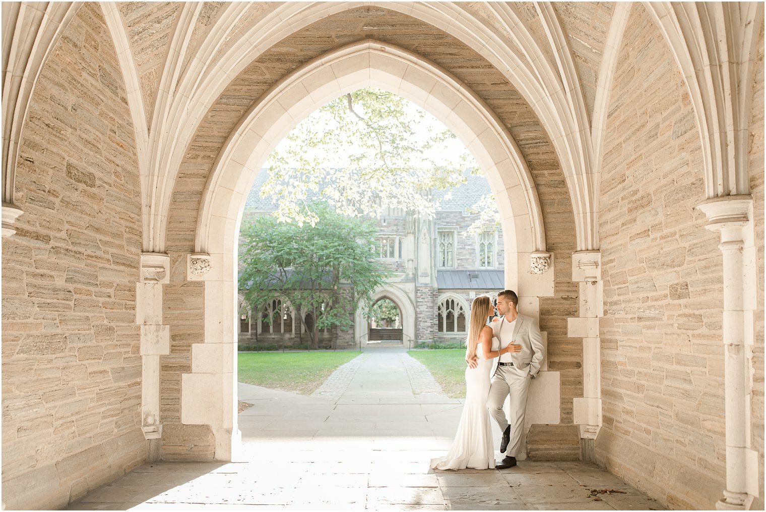 bride leans against groom standing in archway at Rockefeller College 