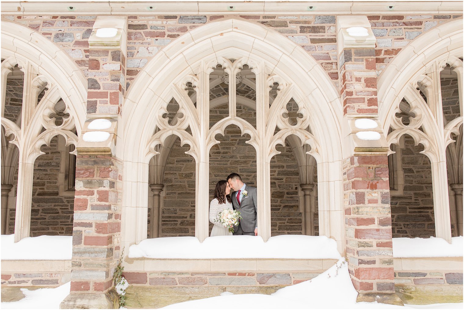 bride and groom touch heads in window of Rockefeller College during wedding portraits in the snow