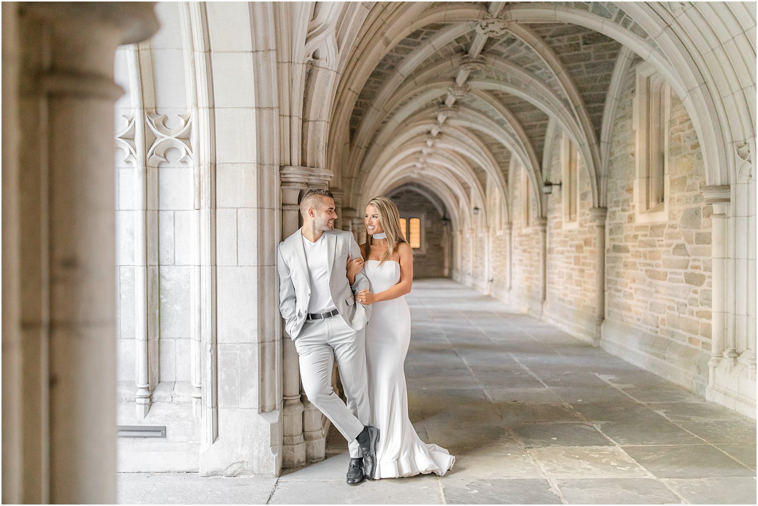bride and groom lean against pillar of Rockefeller College during engagement photos at Princeton University